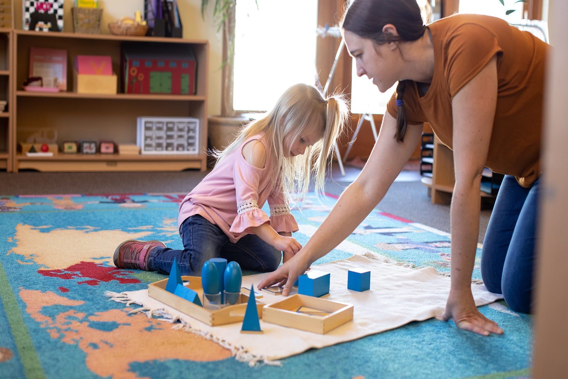 Montessori teacher guiding child with geometric sensorial materials on classroom floor
