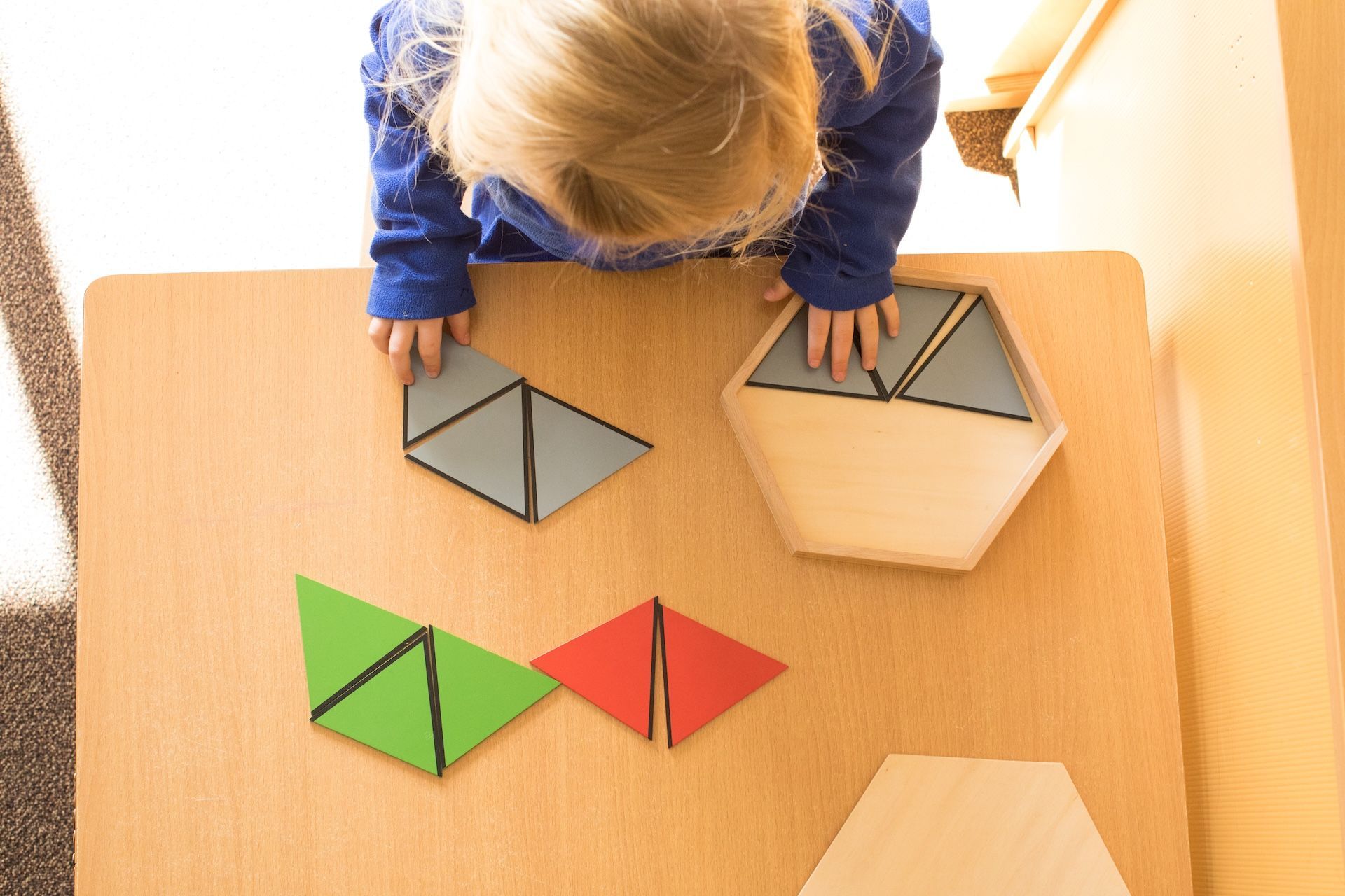Child arranging colorful geometric tiles on a wooden table