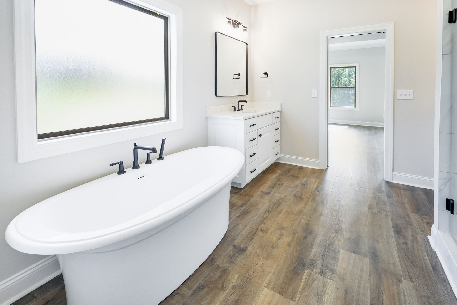 Bathroom with a white freestanding tub, vanity, dark fixtures, and wood-look flooring.