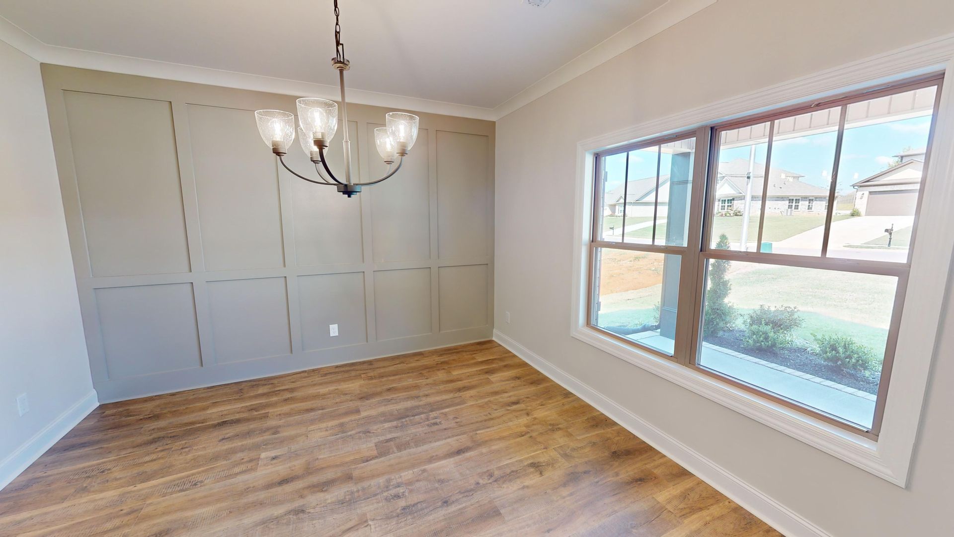 Dining room with wood floors, paneled wall, chandelier, and a large window.