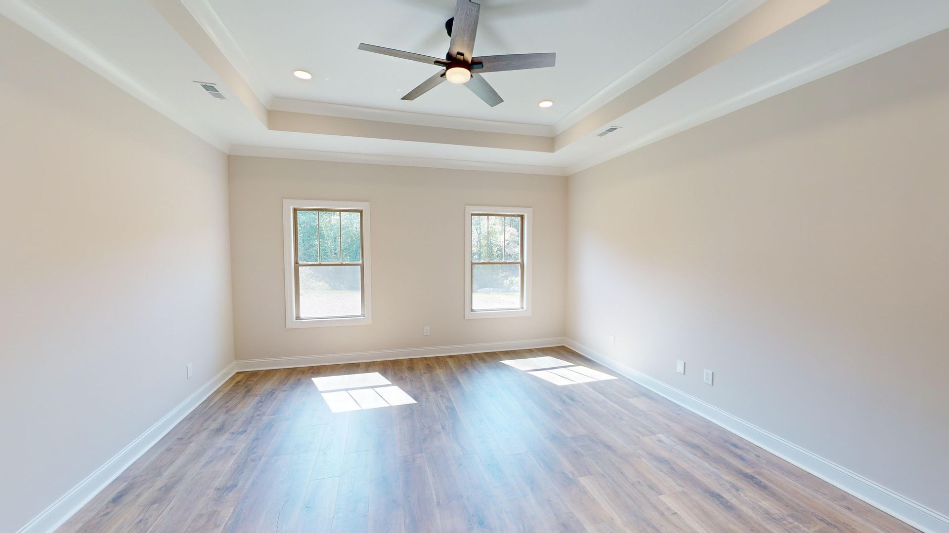 Empty bedroom with hardwood floors, two windows, and a ceiling fan.