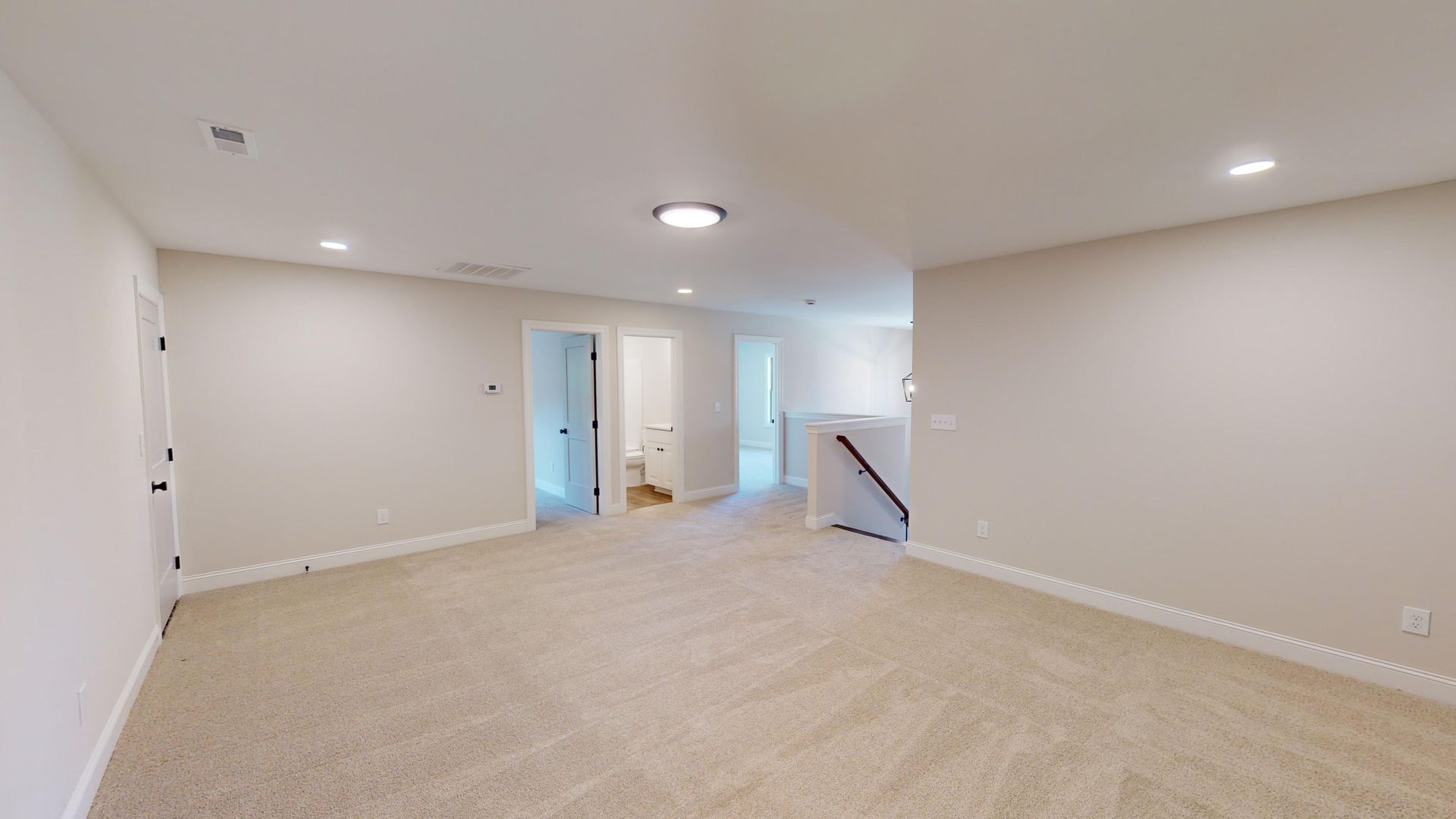 Empty room with beige carpet, recessed lighting, and doorways.