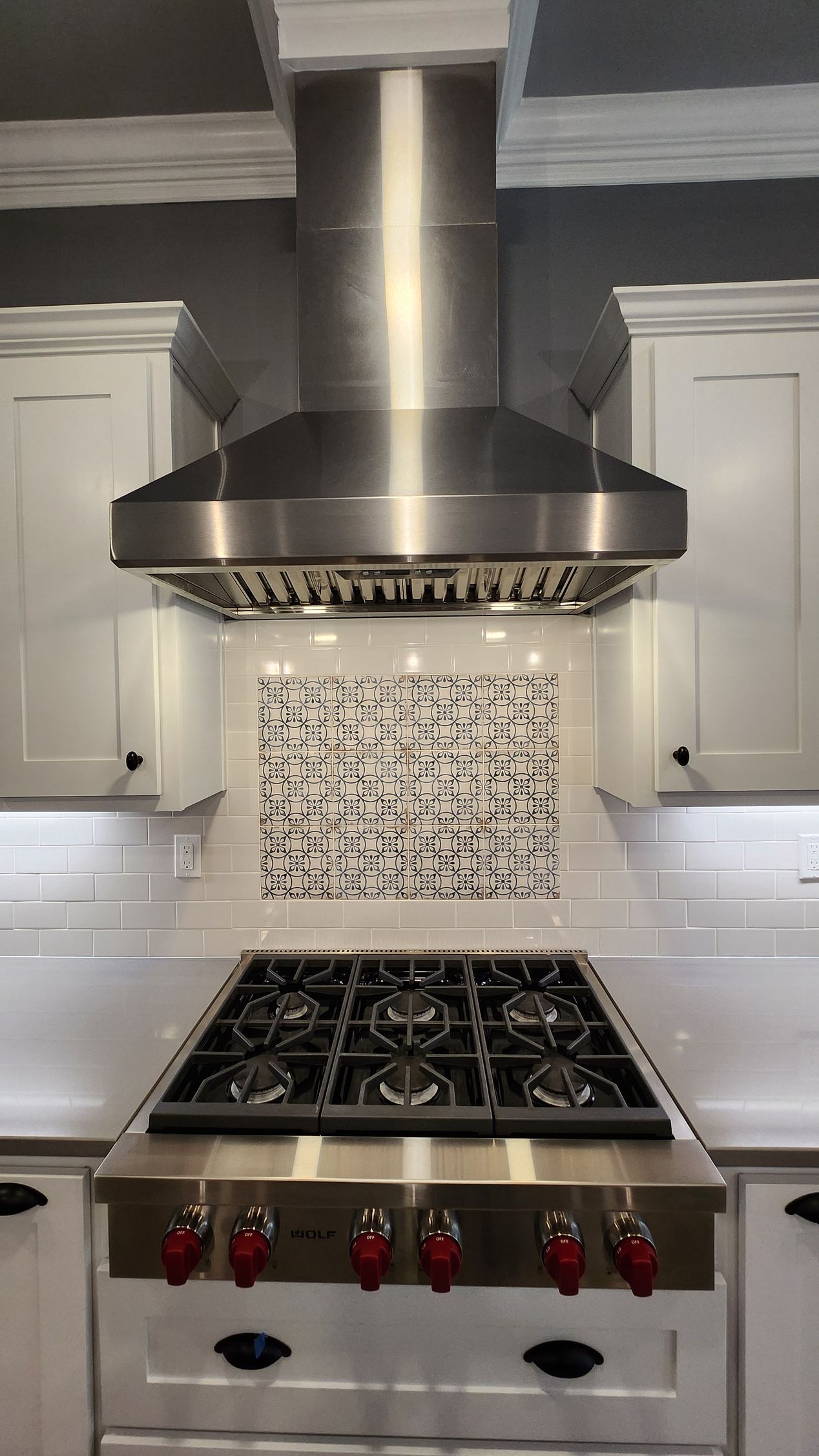 Stainless steel range hood over a gas range with red knobs in a white kitchen.