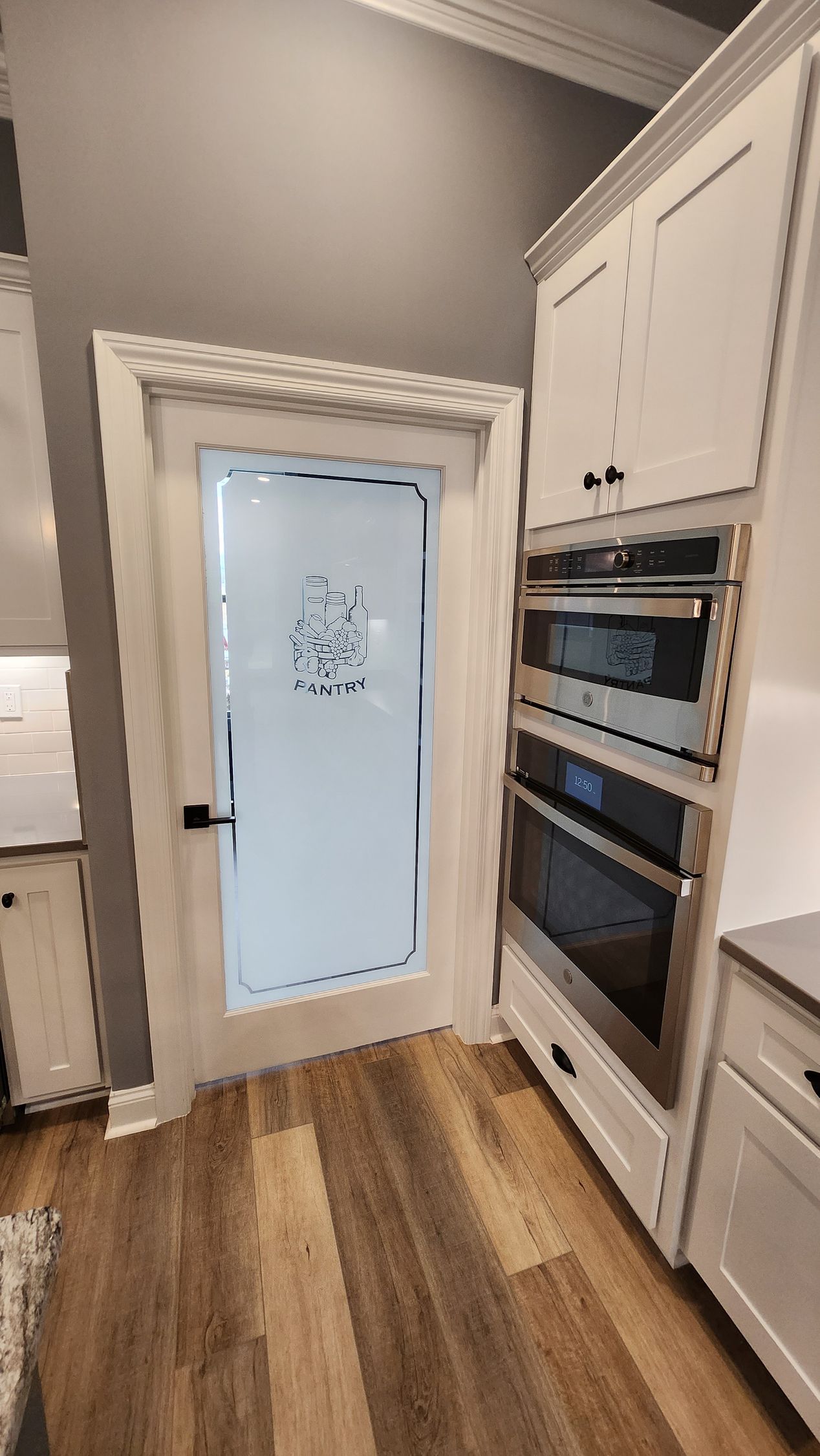 A pantry door with frosted glass and an adjacent tall cabinet with built-in ovens in a kitchen.