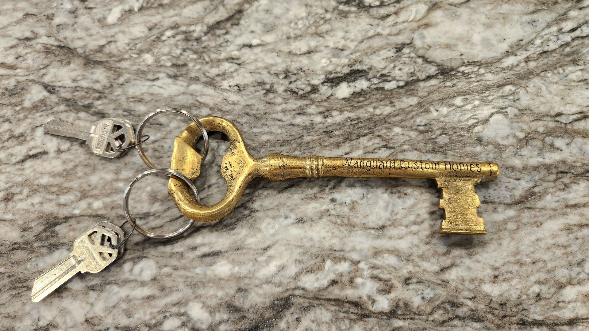 Gold, ornate key with small keys on a ring, resting on a speckled, gray surface.