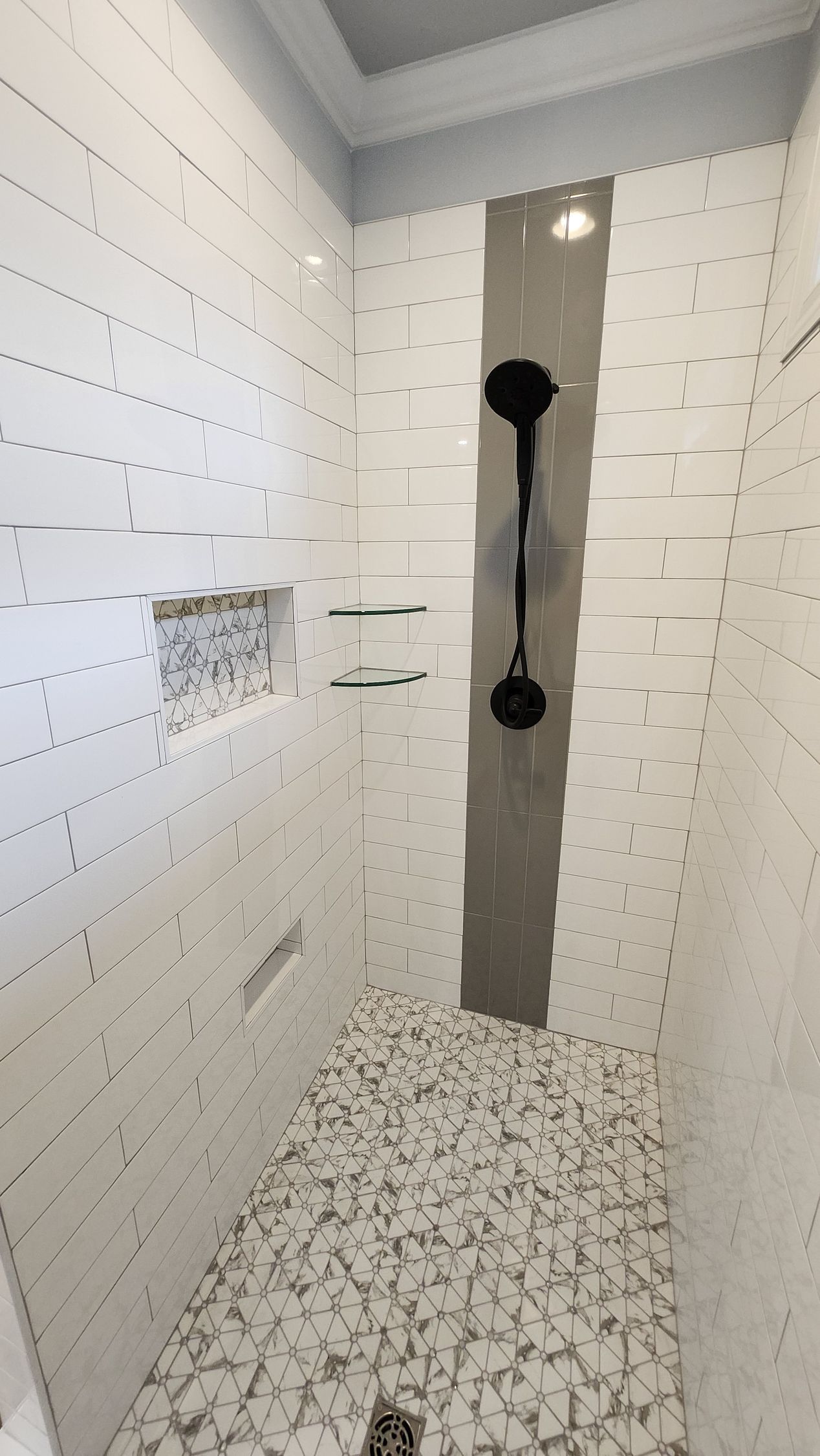 White tiled shower with a gray accent strip and black showerheads. Pebble floor.