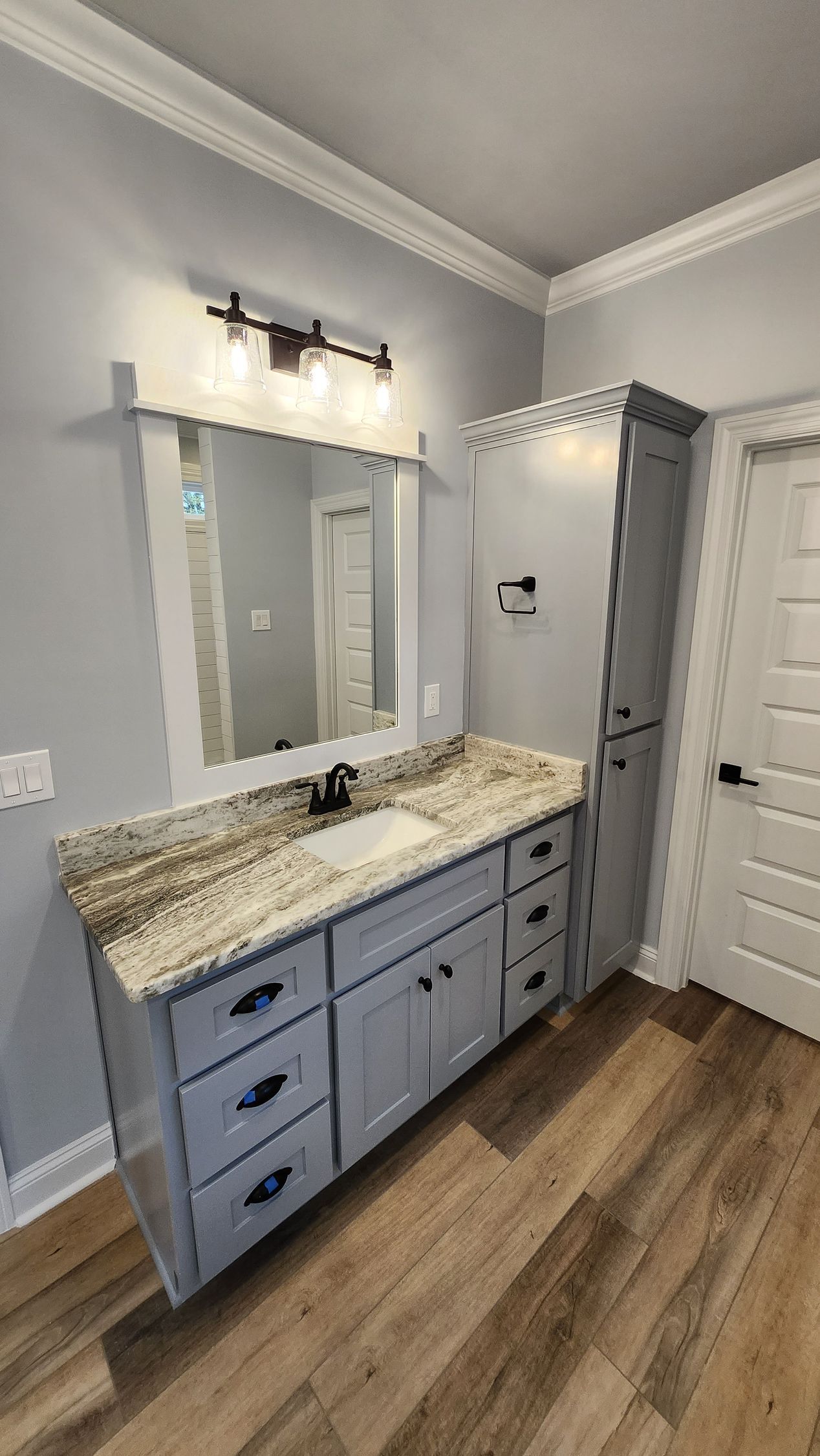 Bathroom with gray vanity, granite countertop, mirror, and tall storage cabinet.