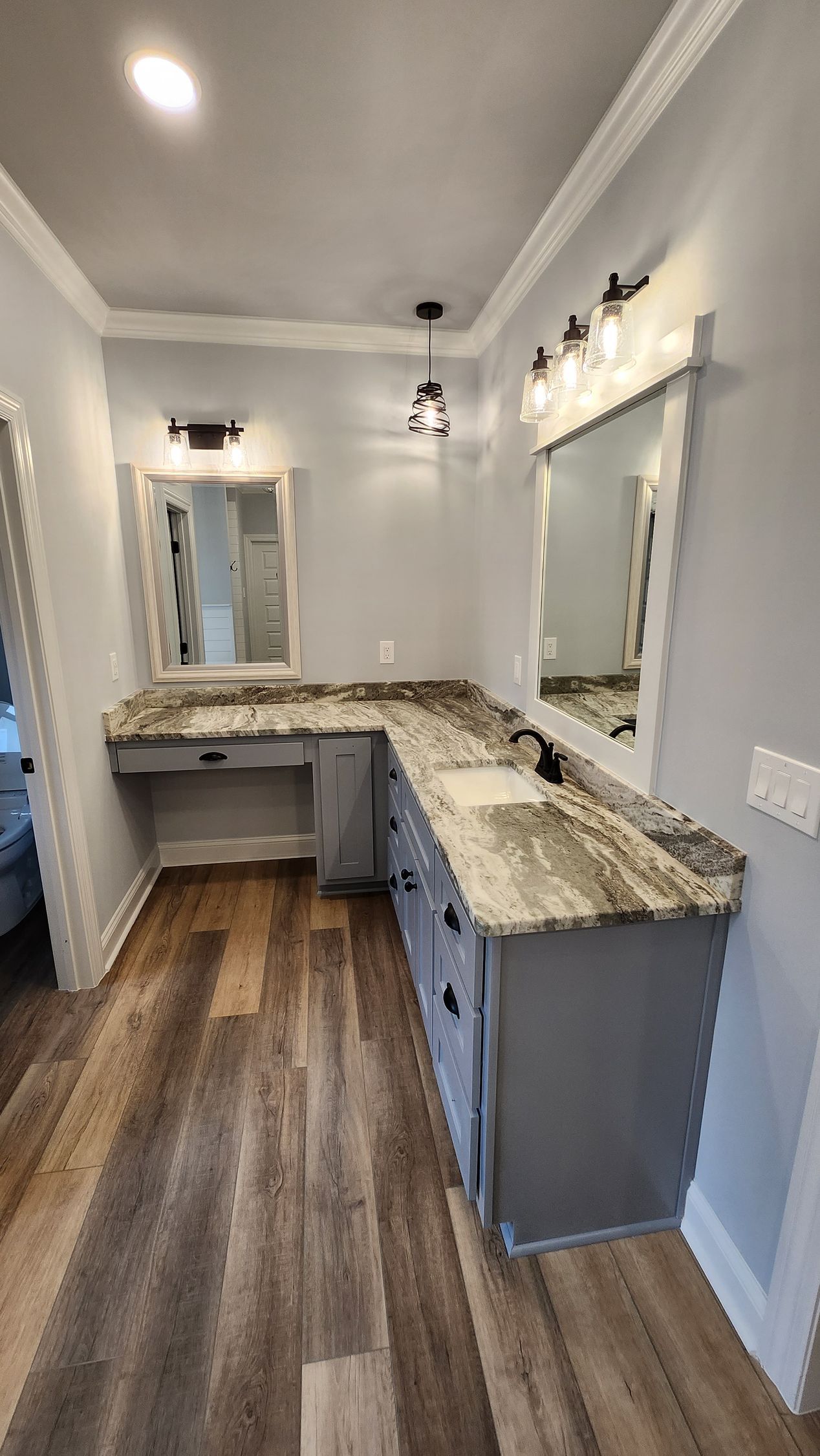Gray bathroom vanity with granite countertop, mirrors, and lighting against a light gray wall.