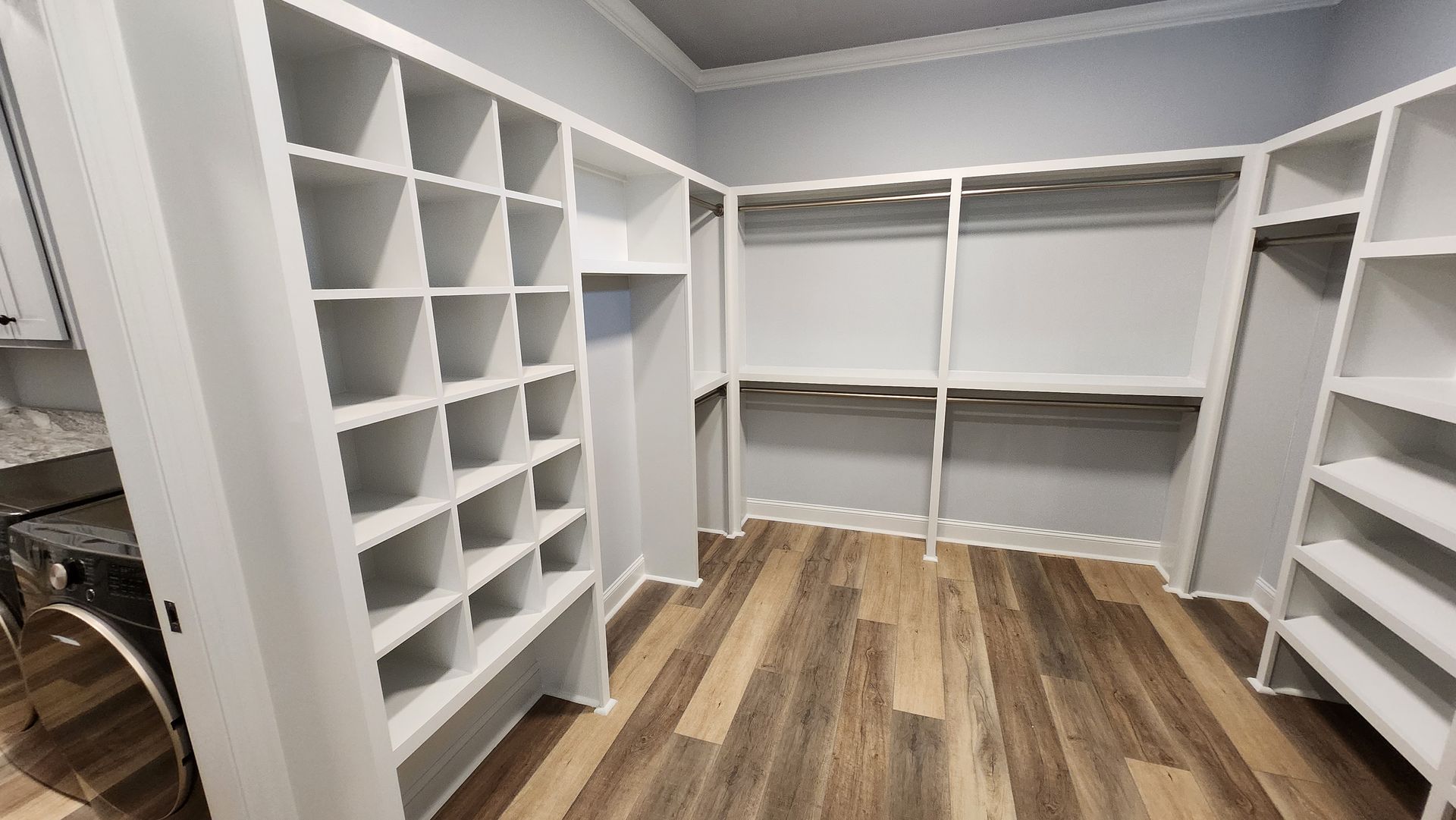 Empty walk-in closet with white shelving and wooden floor.