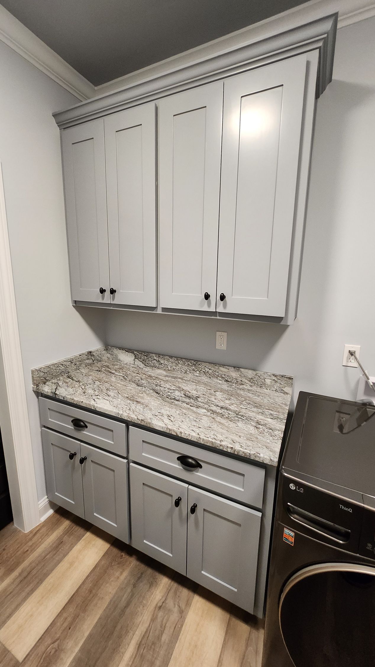 Gray laundry room cabinets with granite countertop, black hardware, and a washing machine.
