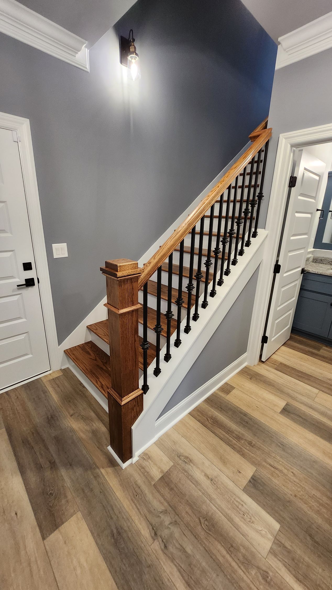 Wooden staircase with black metal spindles and gray walls, in a home setting.