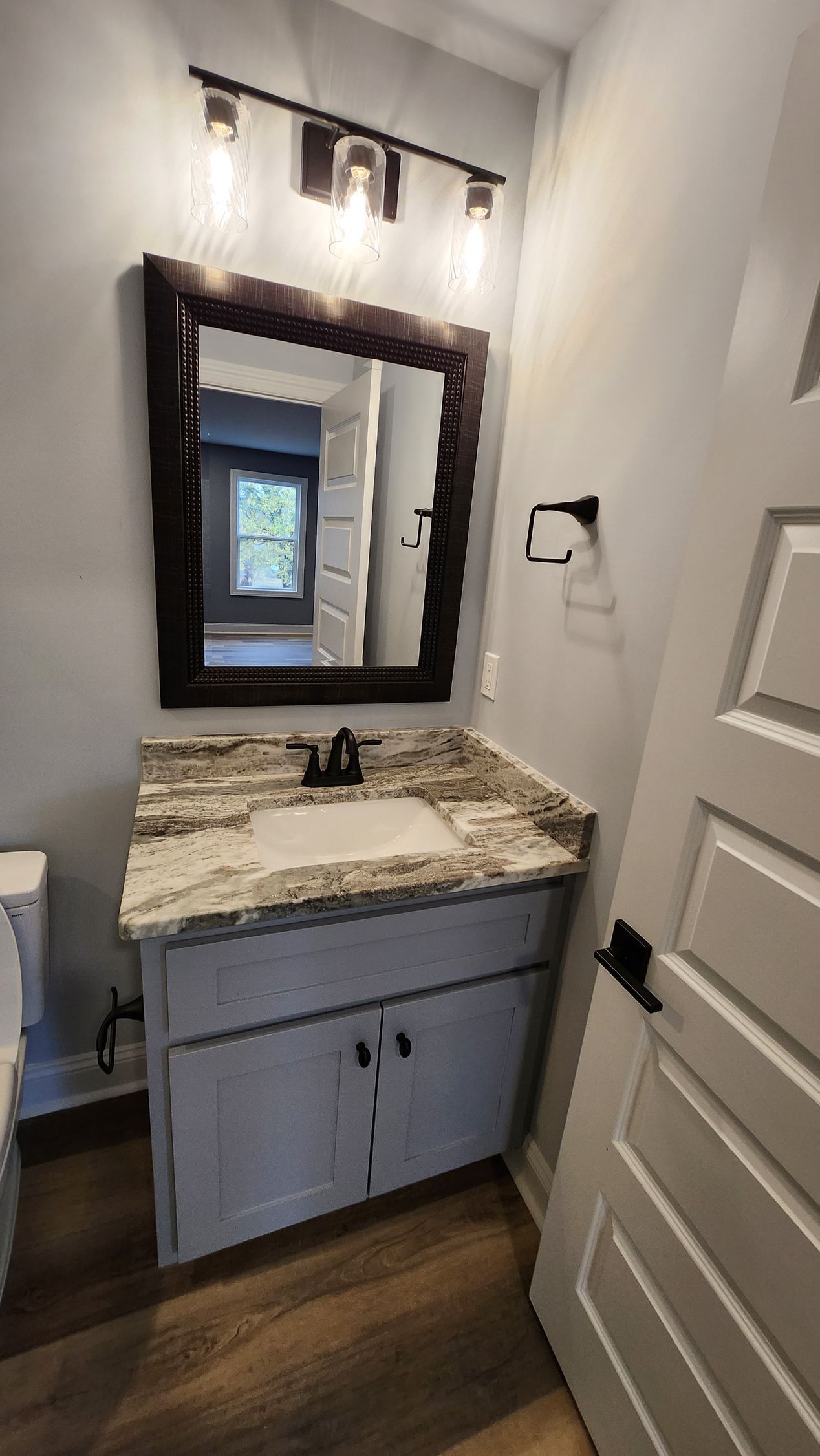 Bathroom with white vanity, granite countertop, mirror, and light fixture.