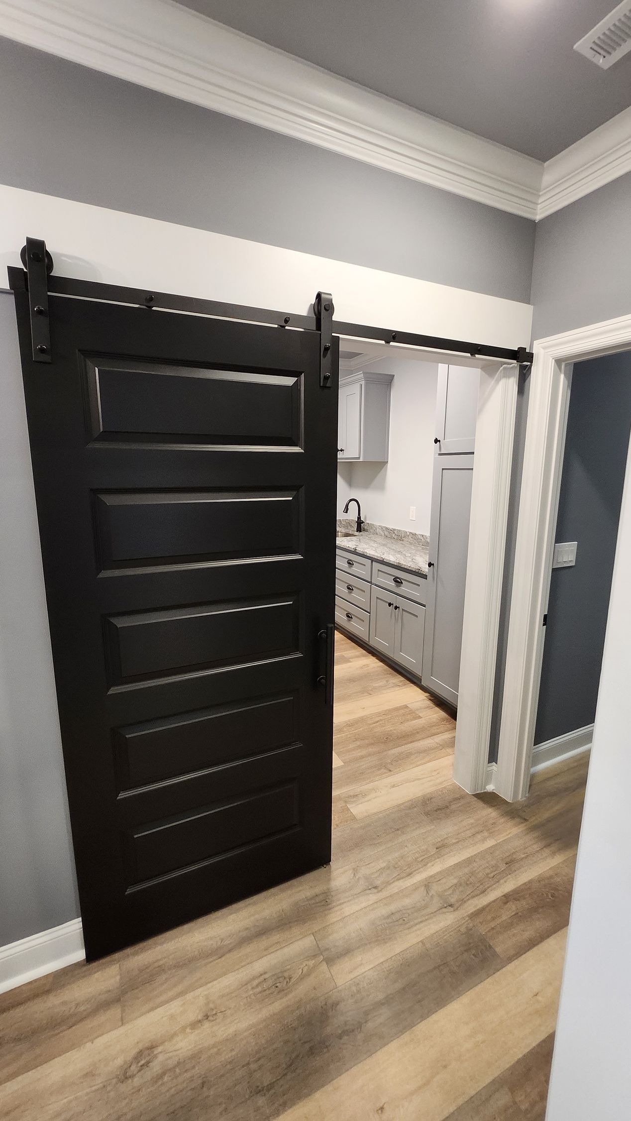 Black sliding barn door open, revealing a kitchen with gray cabinets and white appliances.