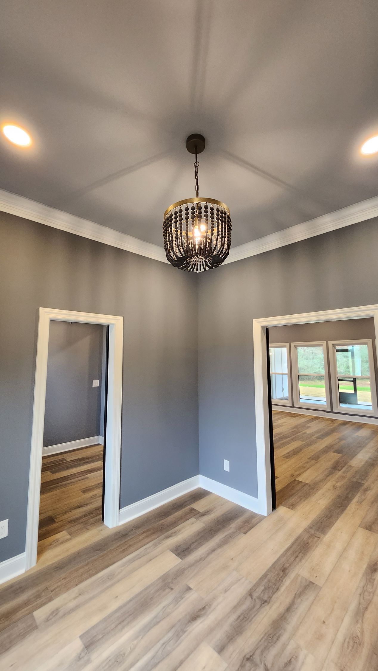 A room with gray walls, light wood flooring, white trim, and a chandelier; doors lead to other spaces.