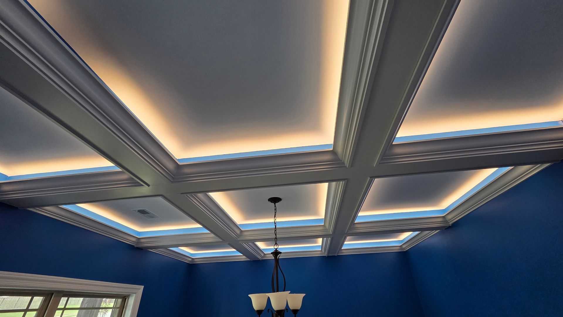 Coffered ceiling with integrated warm lighting, blue walls, and a chandelier.