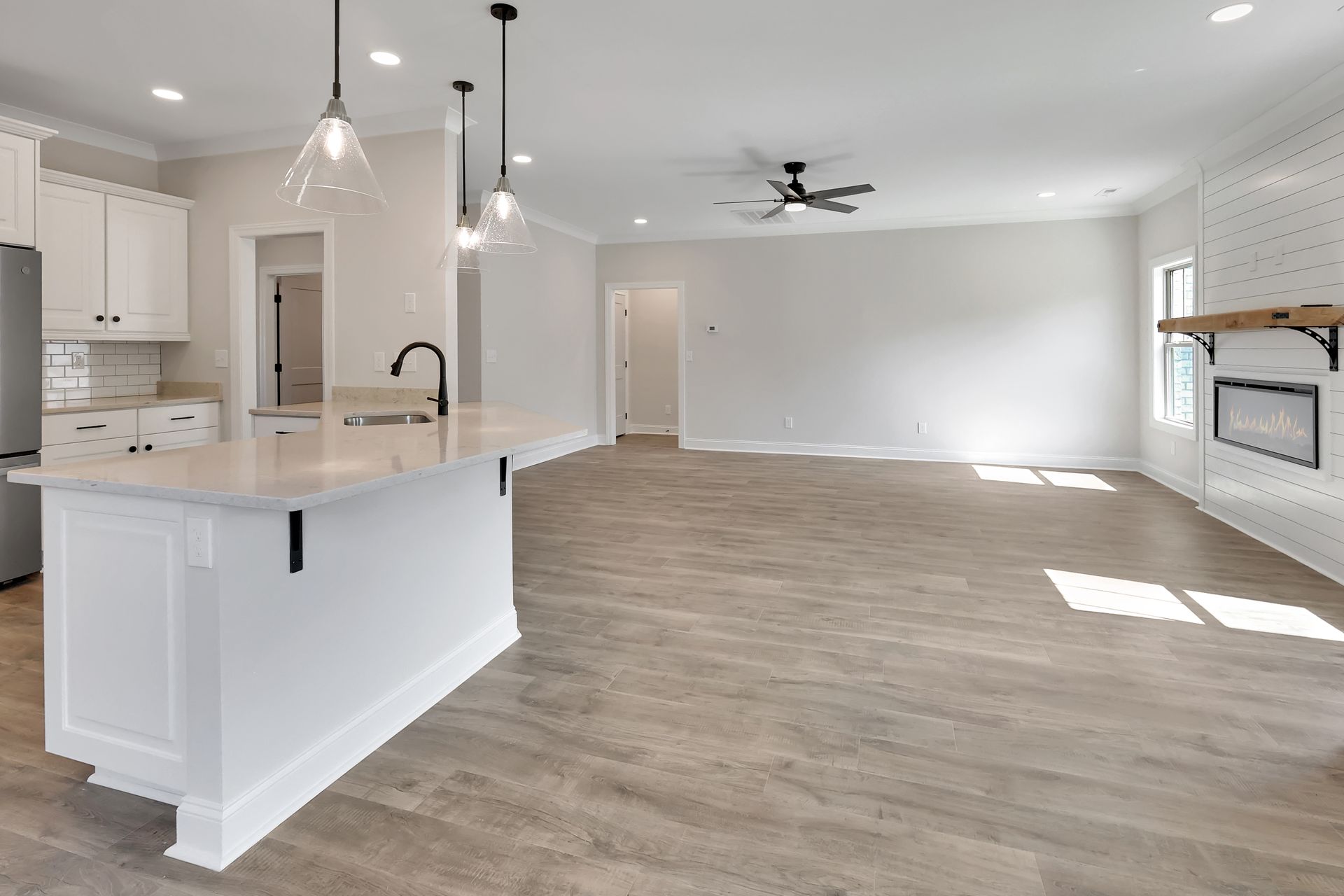Open-concept kitchen and living area with white walls, island, and wood-look flooring. Fireplace on the right.