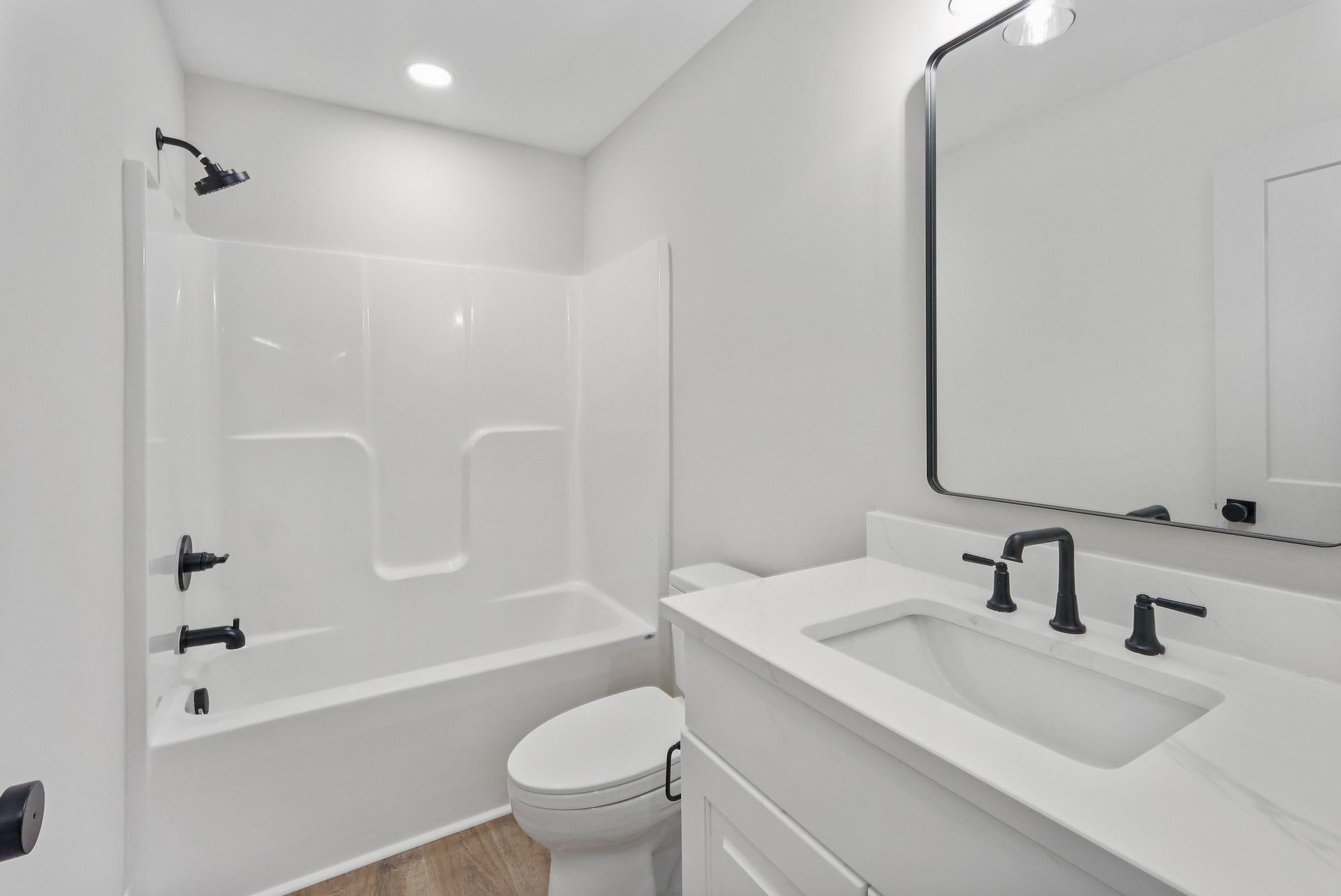 White bathroom with bathtub, toilet, and vanity with black fixtures and mirror.