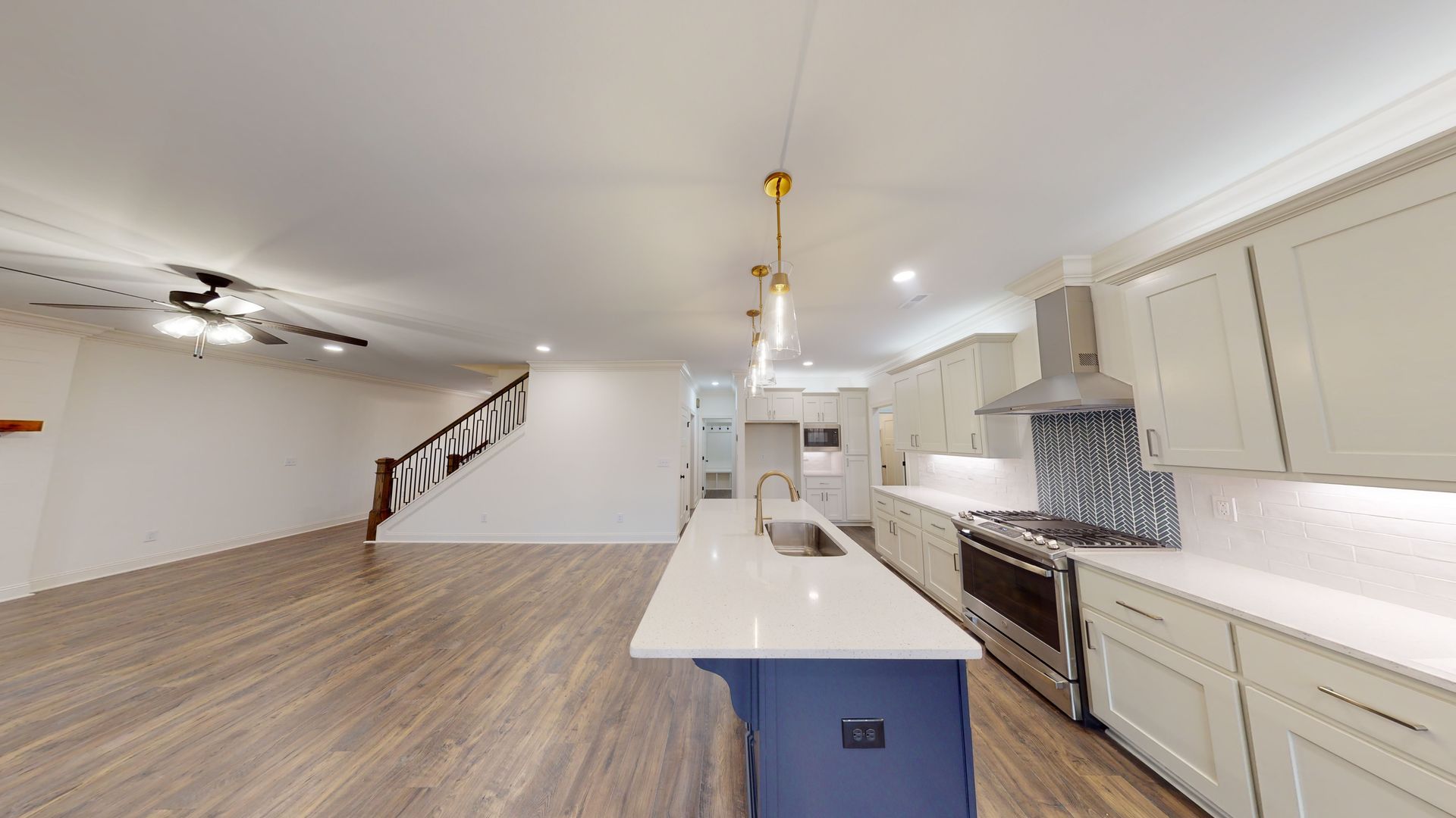 Modern kitchen with white cabinets, blue island, stainless steel appliances, and wooden floors.