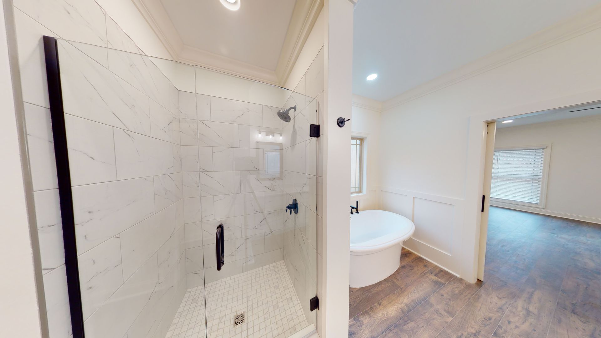 Bathroom with a glass-enclosed shower, a round bathtub, and an open doorway to another room.