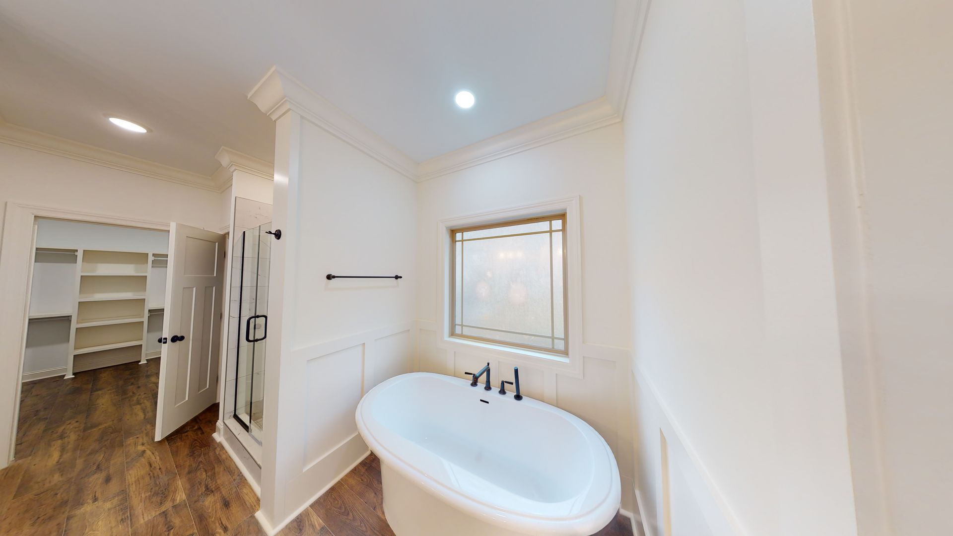 Bathroom with a white bathtub, shower, and walk-in closet with wooden floors.