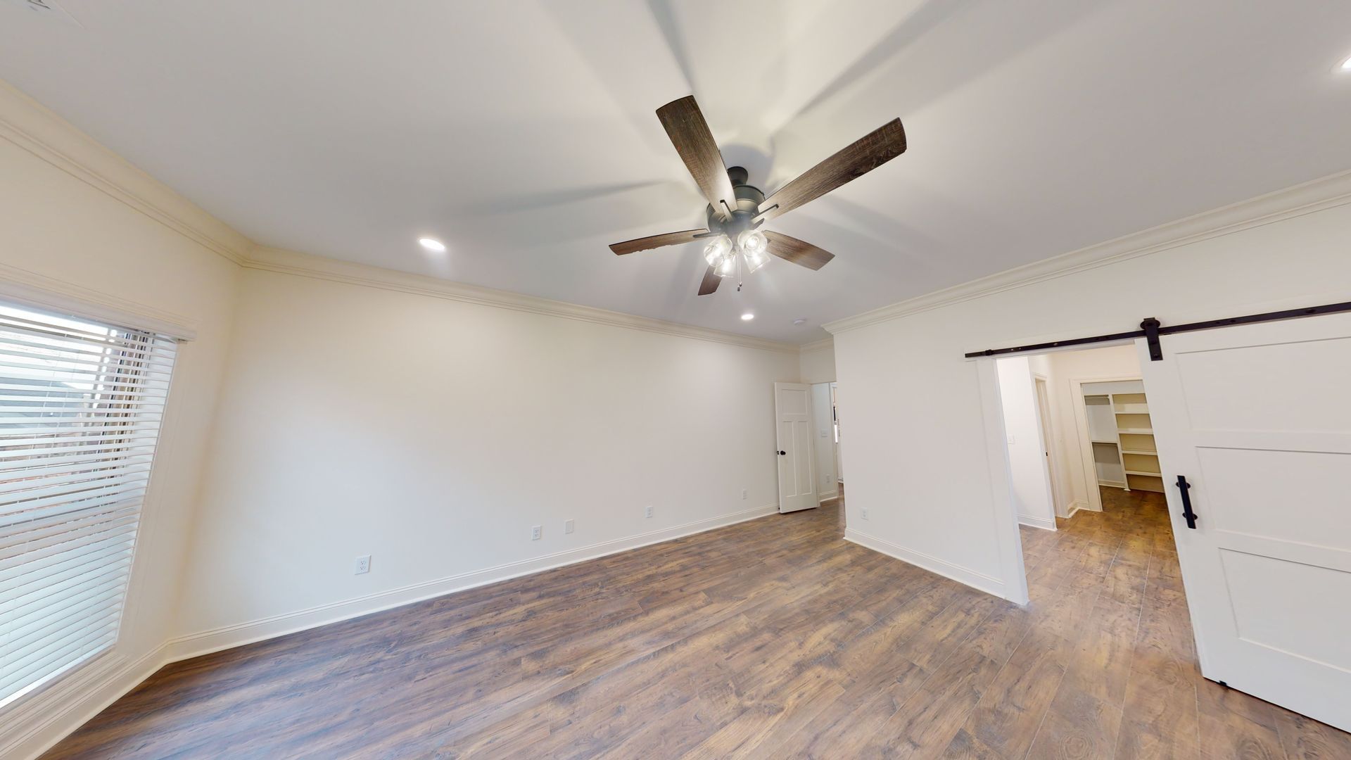 Empty bedroom with hardwood floors, a sliding door, and a ceiling fan.