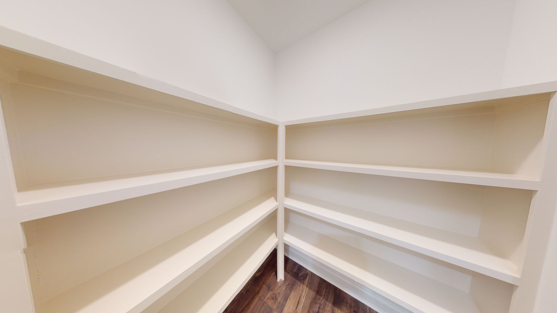 Empty white pantry with multiple shelves and dark wood flooring.
