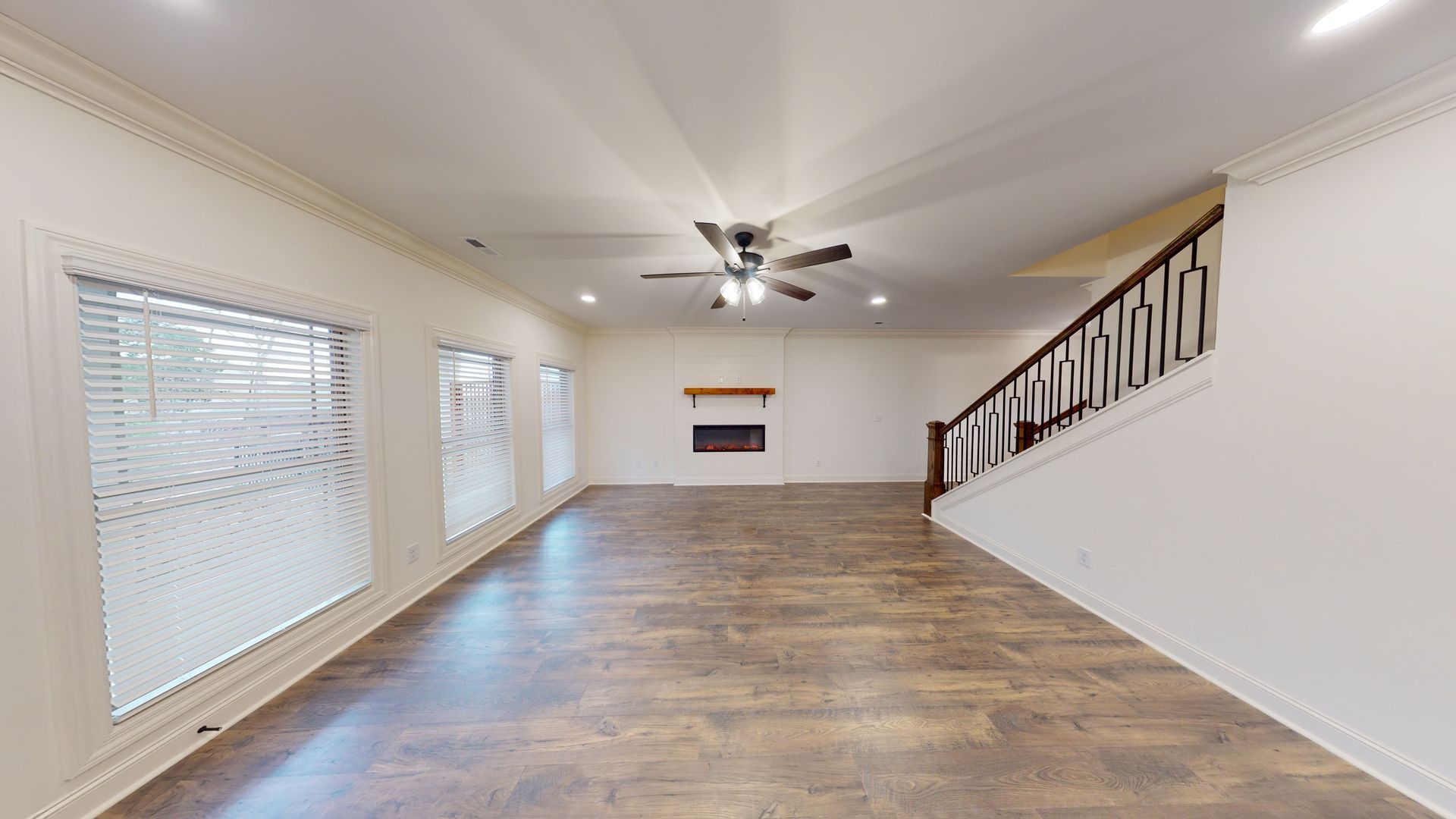 Spacious living room with hardwood floors, windows, fireplace, and staircase.