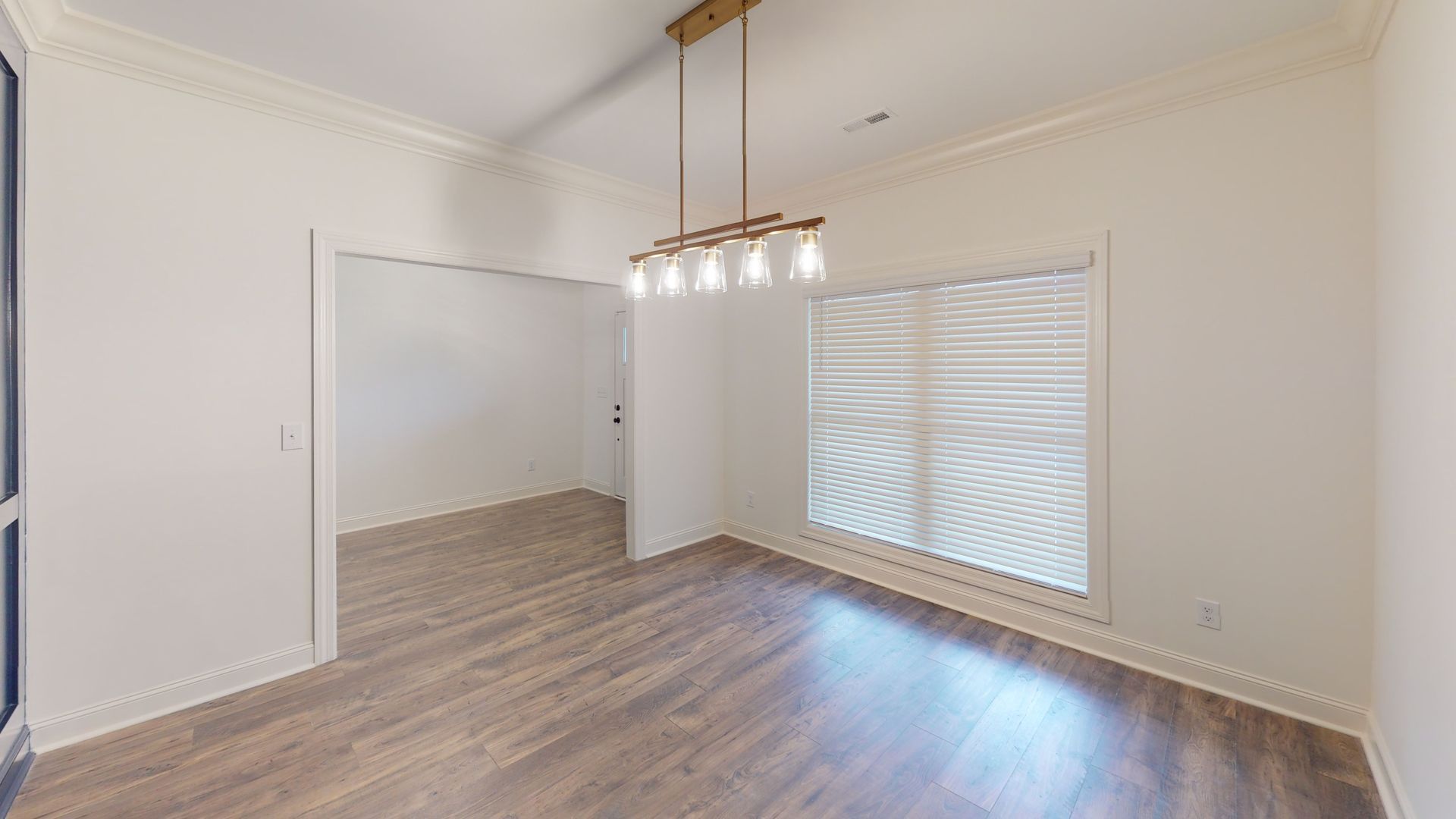 Empty dining room with wood flooring, white walls, and a window with blinds.