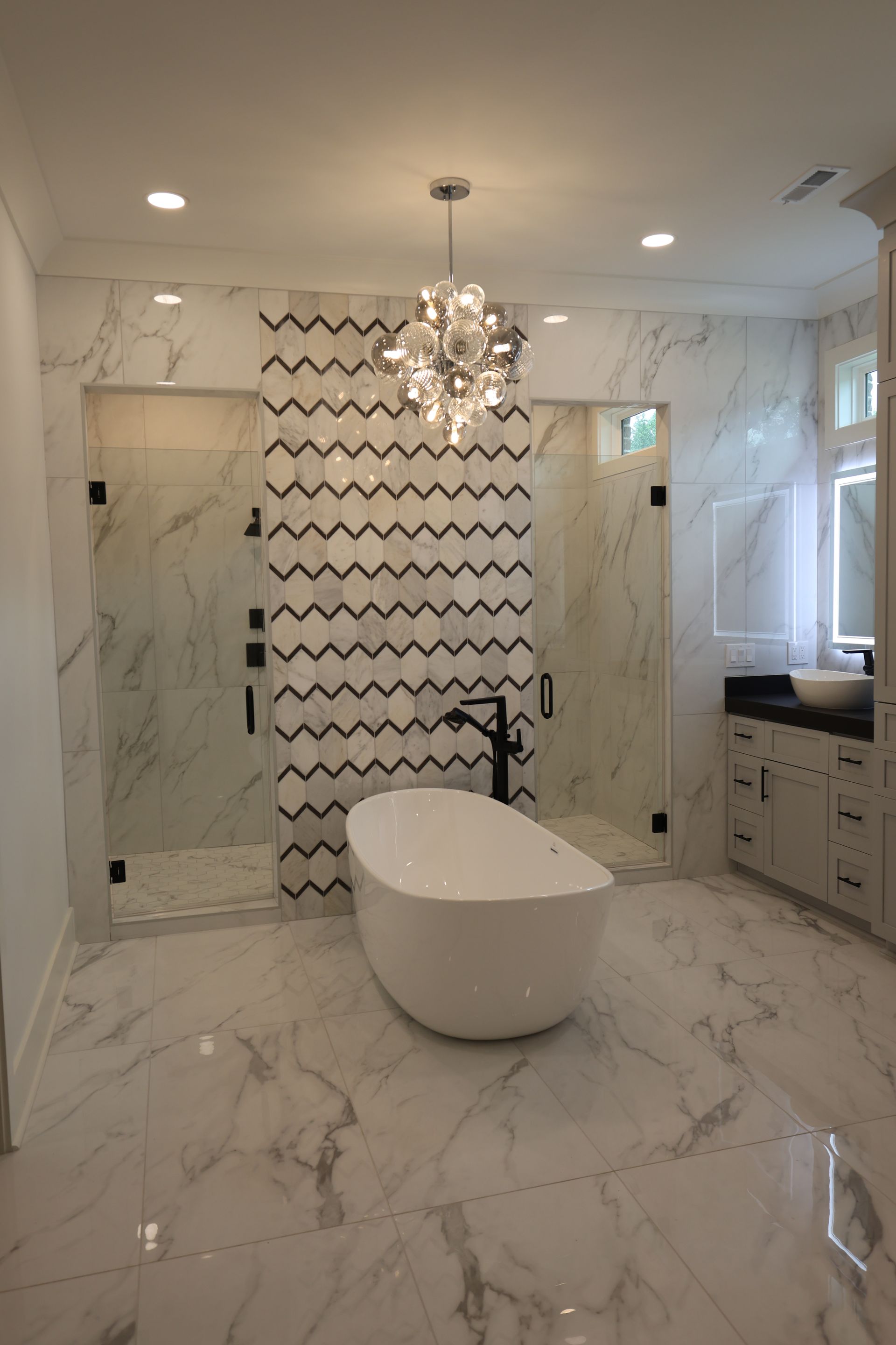 Spacious white and black tiled bathroom with a freestanding tub, glass showers, and a chandelier.