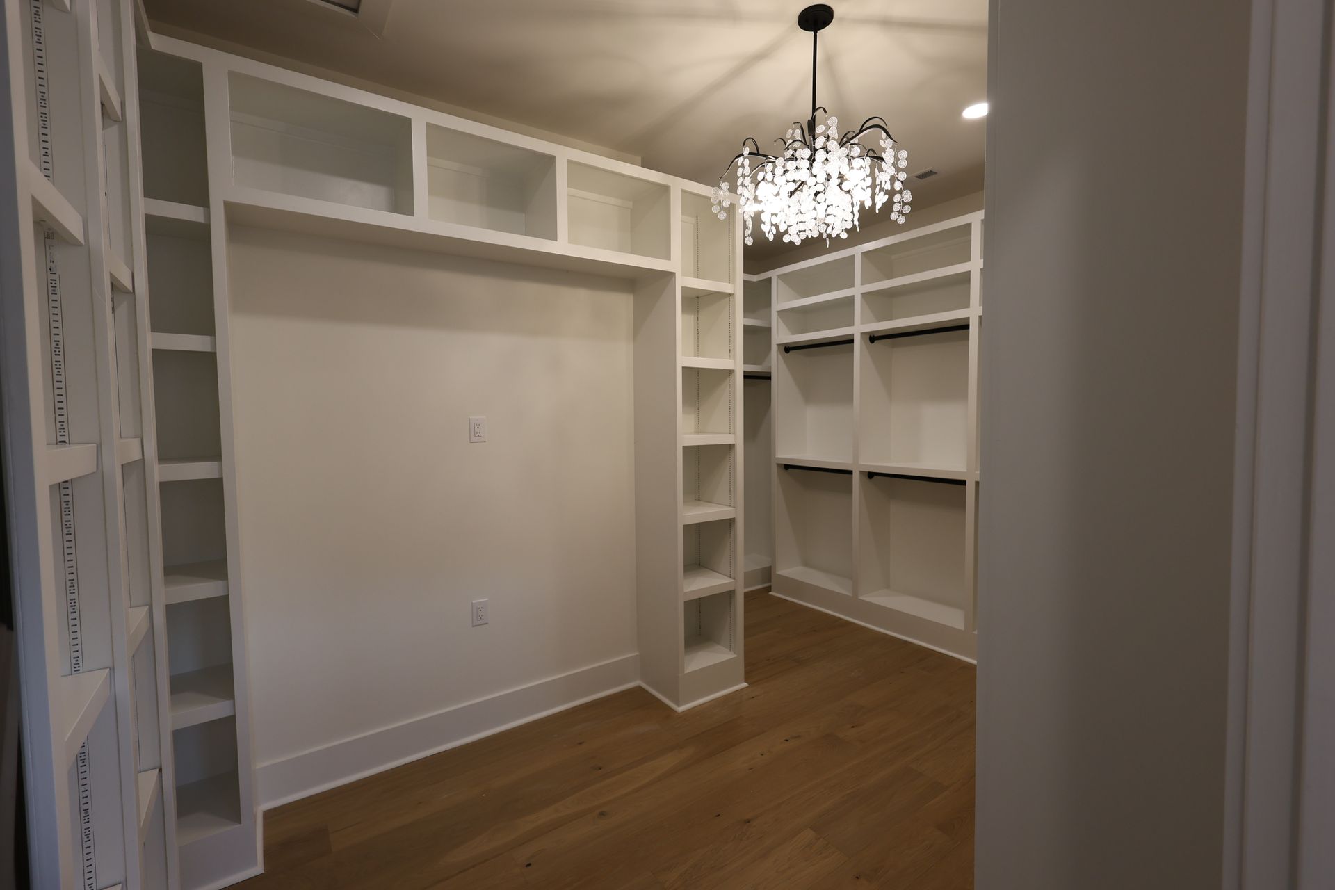 White walk-in closet with shelves and a chandelier; light wood floor.