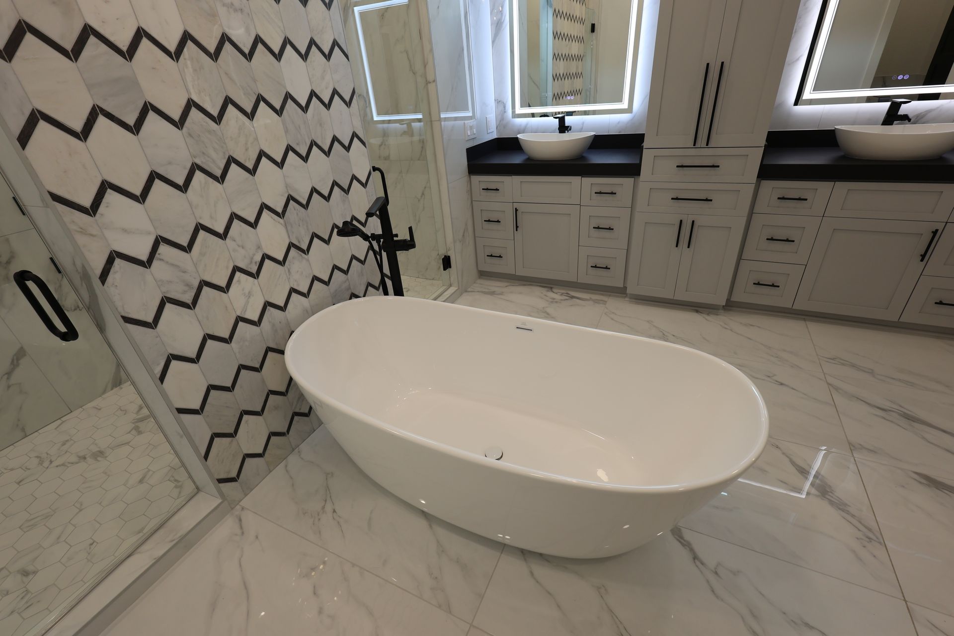 Modern bathroom with a white oval tub, marble floors, and chevron-patterned shower tiles.
