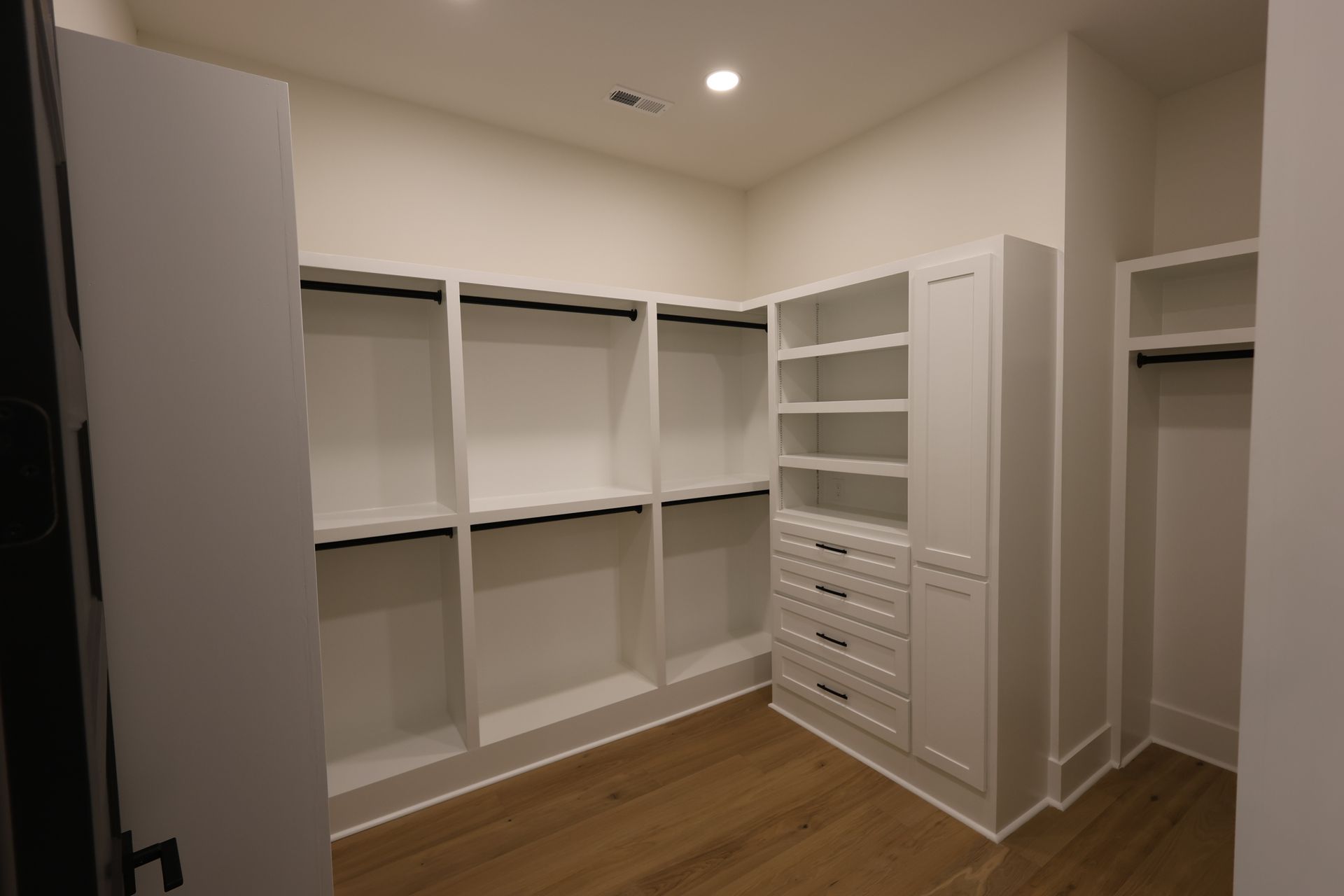 White walk-in closet with shelves, drawers, and hanging rods; wood floor.