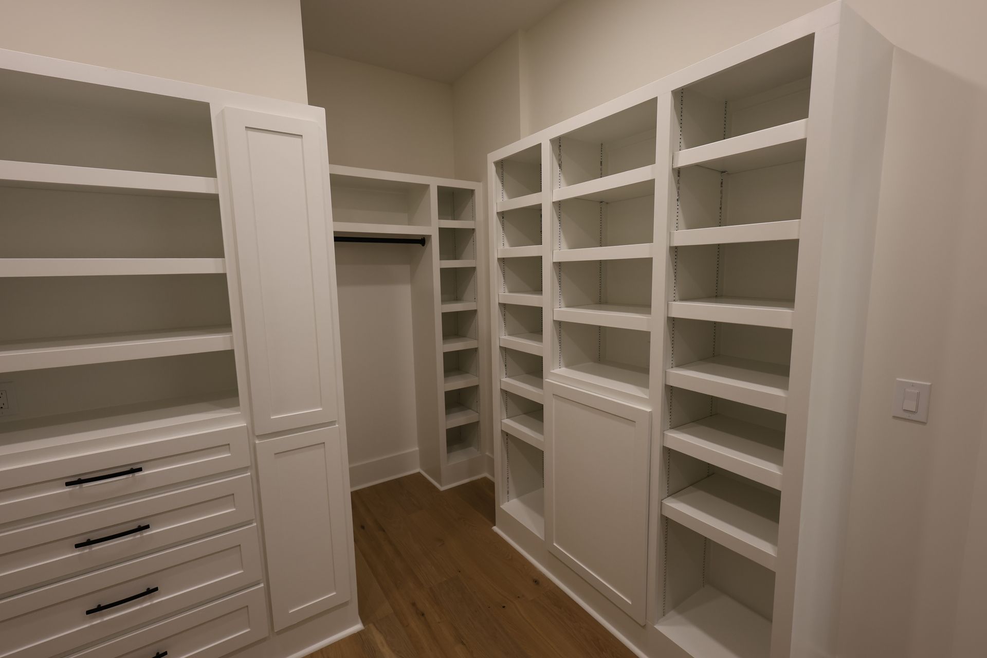 White built-in closet with shelves, drawers, and hanging rod. Wooden floor, neutral walls.