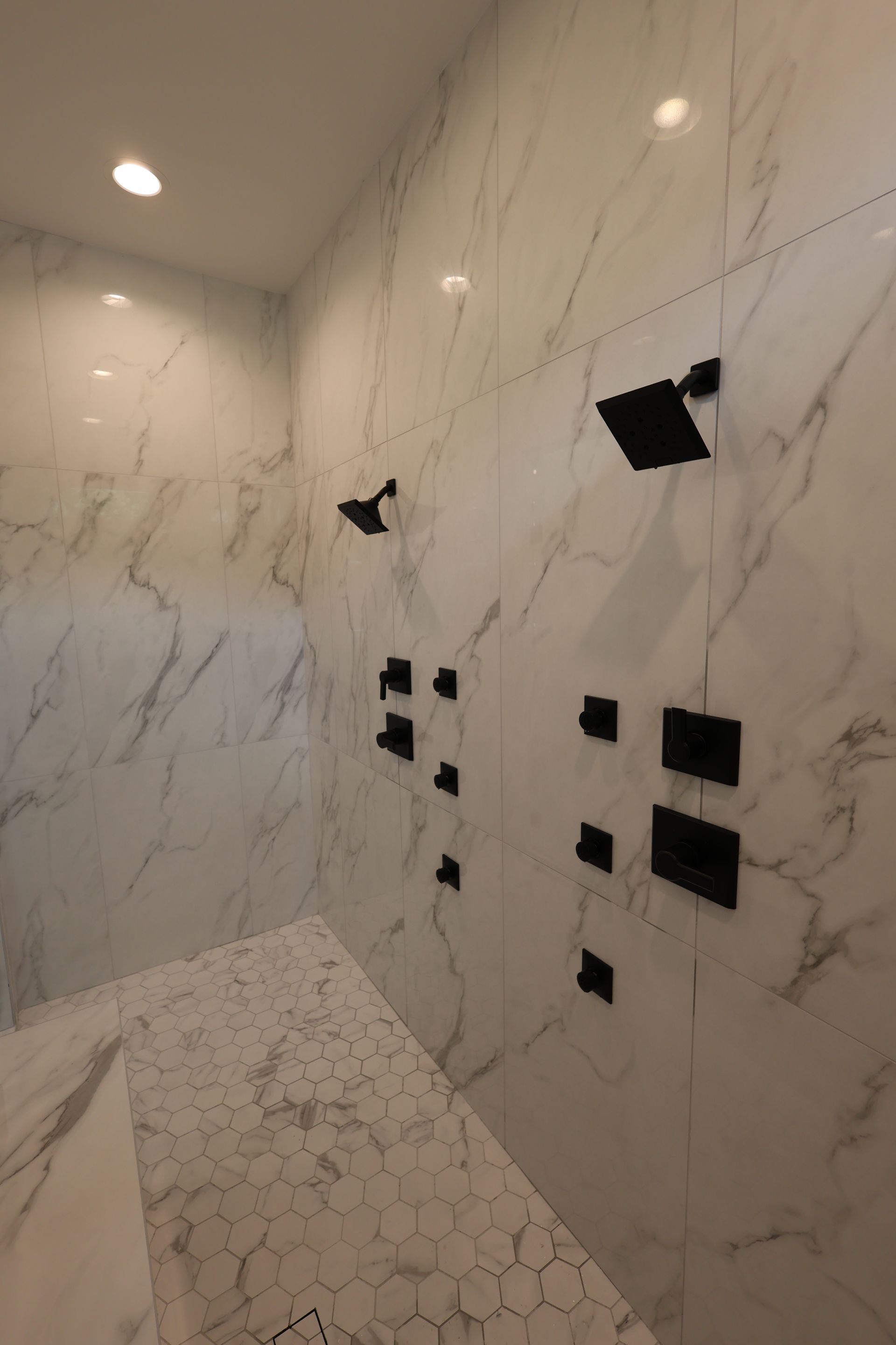 Luxurious shower with white marble walls and multiple black showerheads and body sprays.