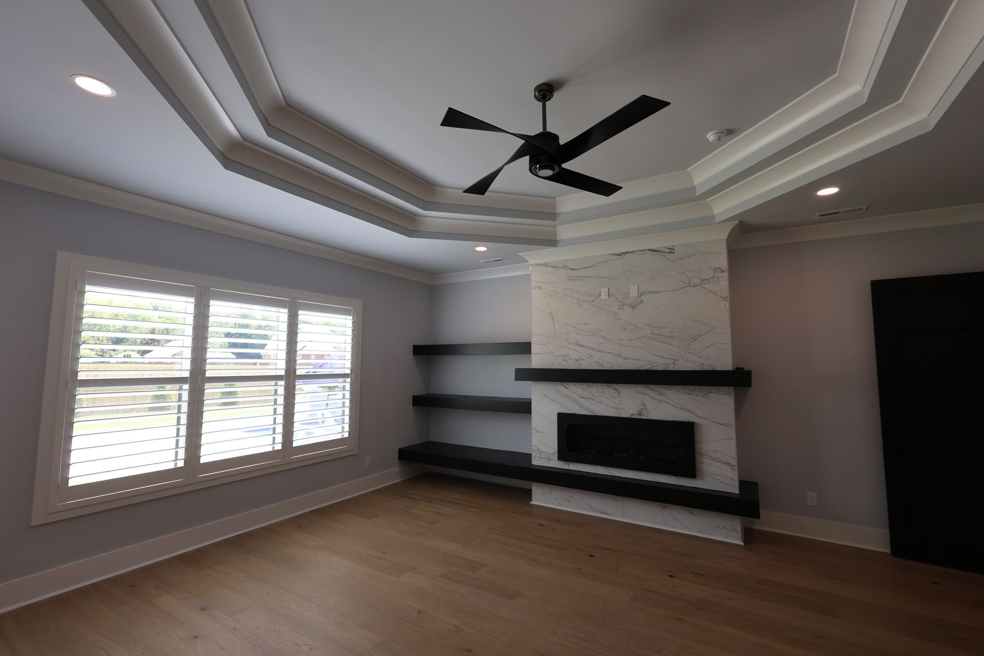 Modern room with light wood floors, window with shutters, decorative ceiling, fireplace and shelving.