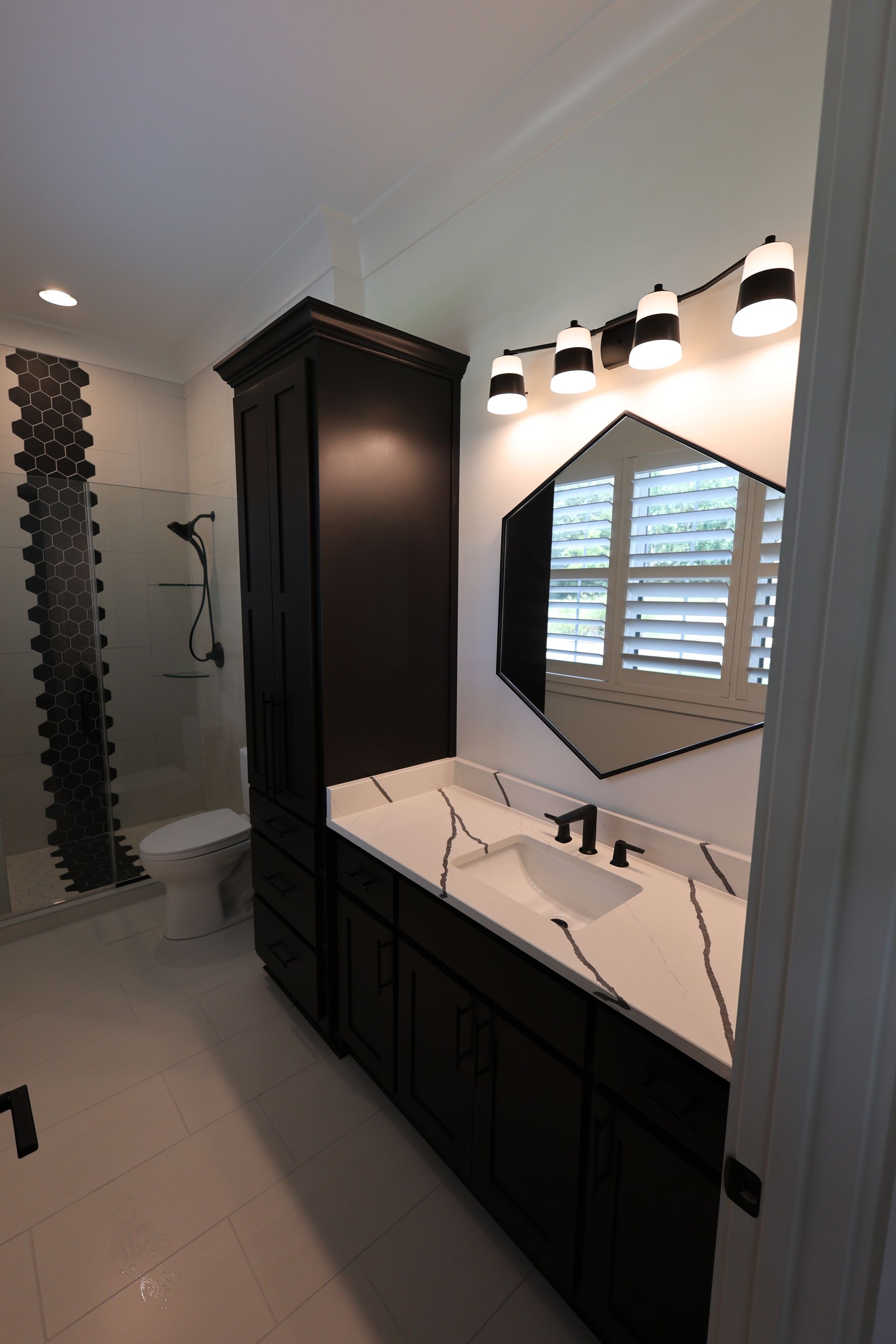 Modern bathroom with black cabinetry, white countertops, hexagon mirror, and decorative tile.