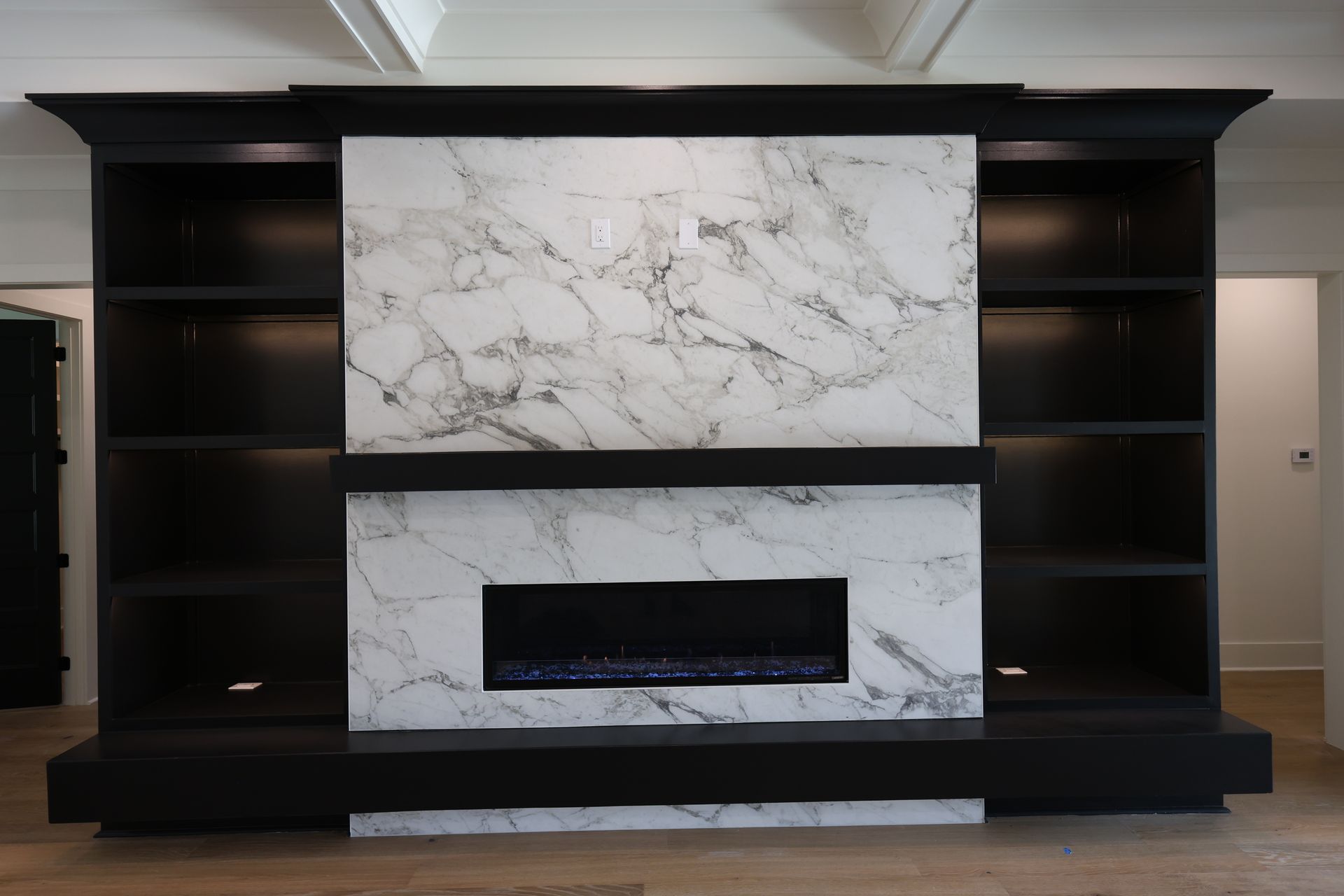 Black built-in entertainment center with marble fireplace, shelving, and recessed lighting against a light-colored wall.