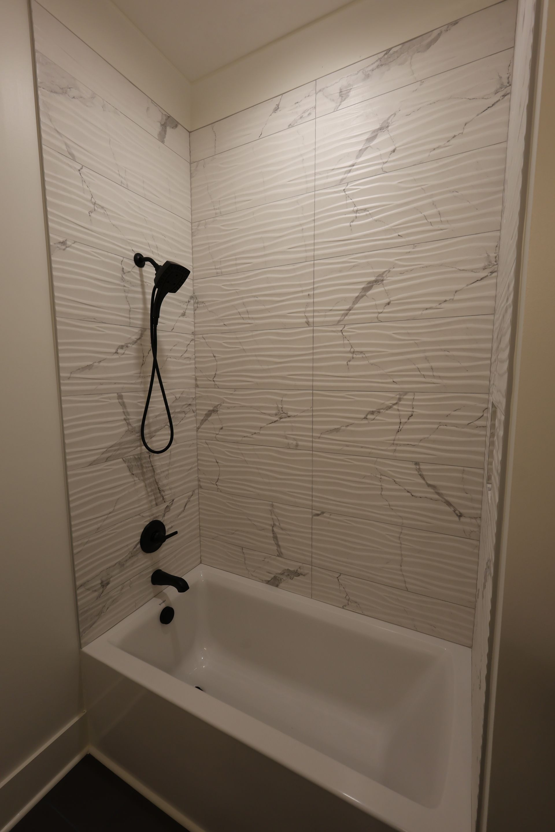 White tiled shower with black shower fixtures, above a white bathtub.