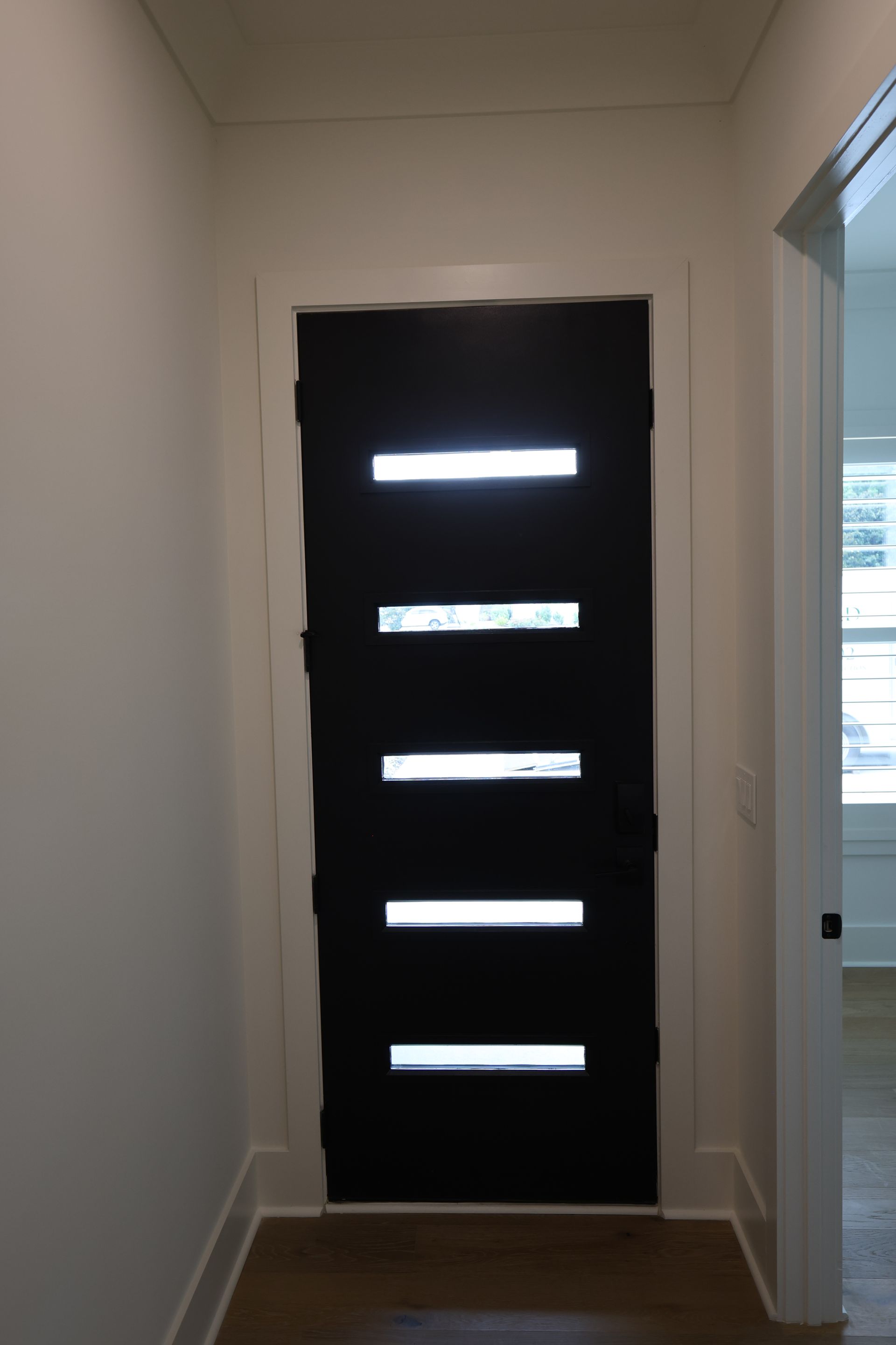 Black front door with five horizontal frosted glass panels, white trim, hallway.