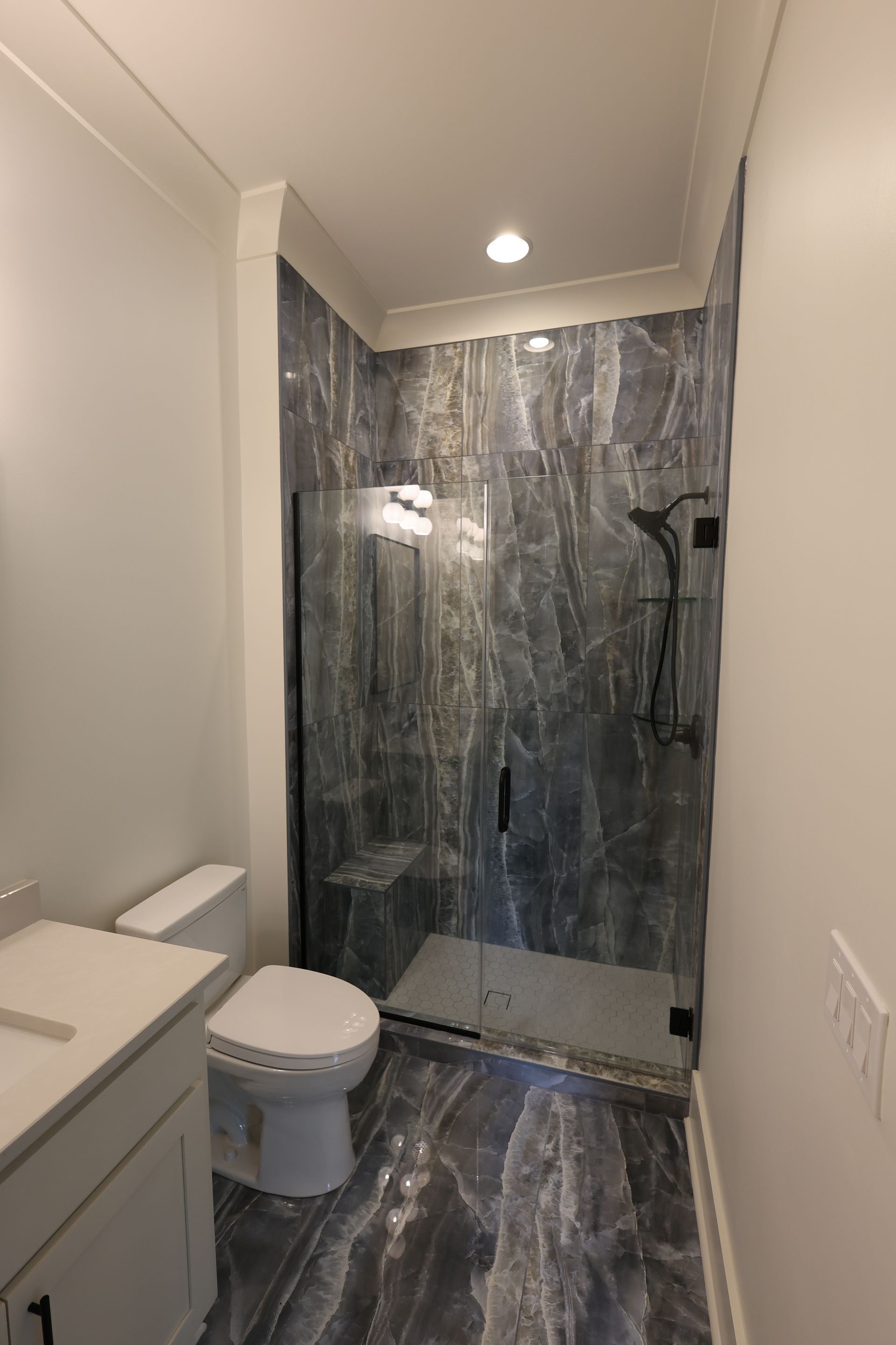 Bathroom with marble-look shower, glass door, toilet, and vanity. Gray and white color scheme.