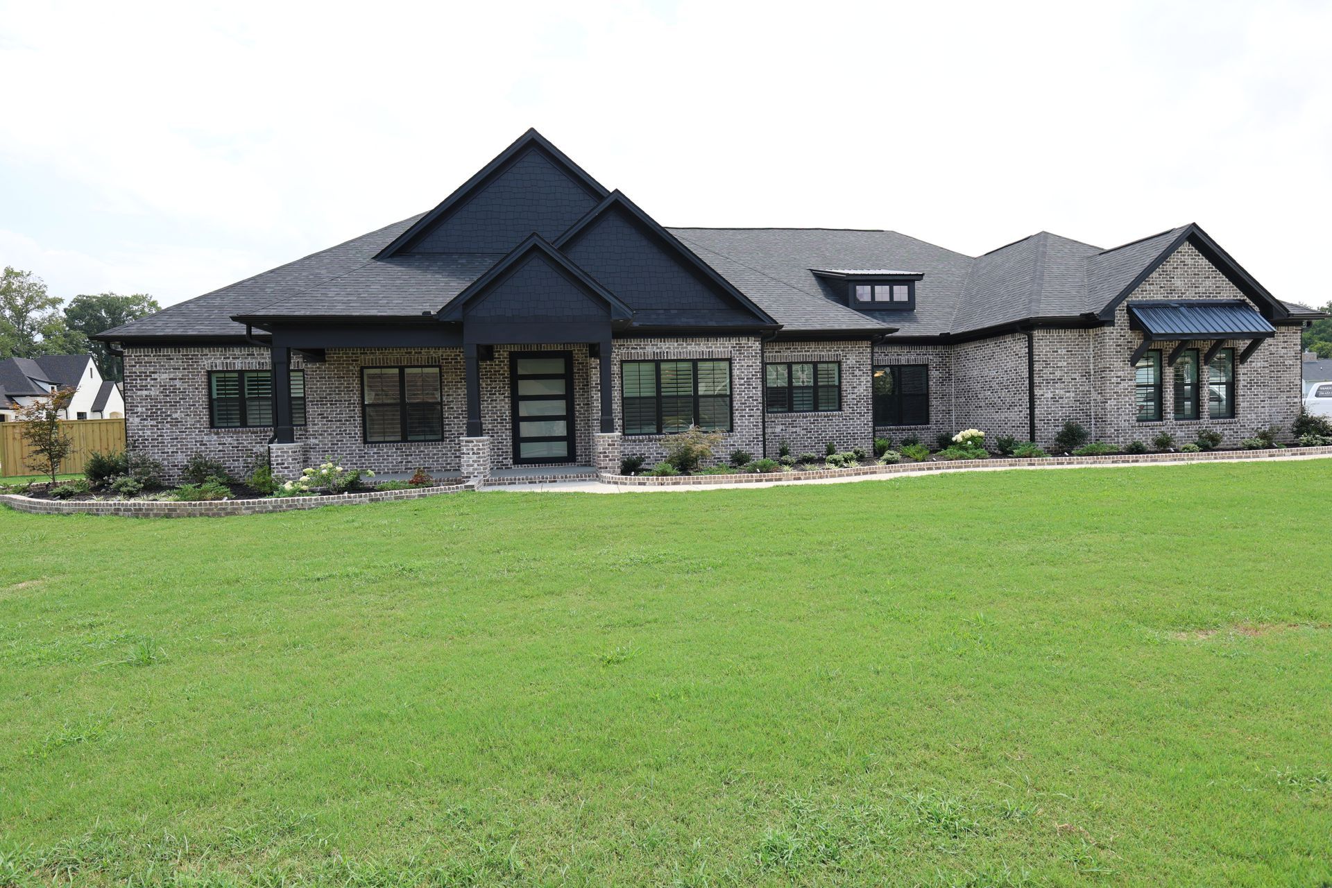 Brick home with dark trim and roof; green lawn.