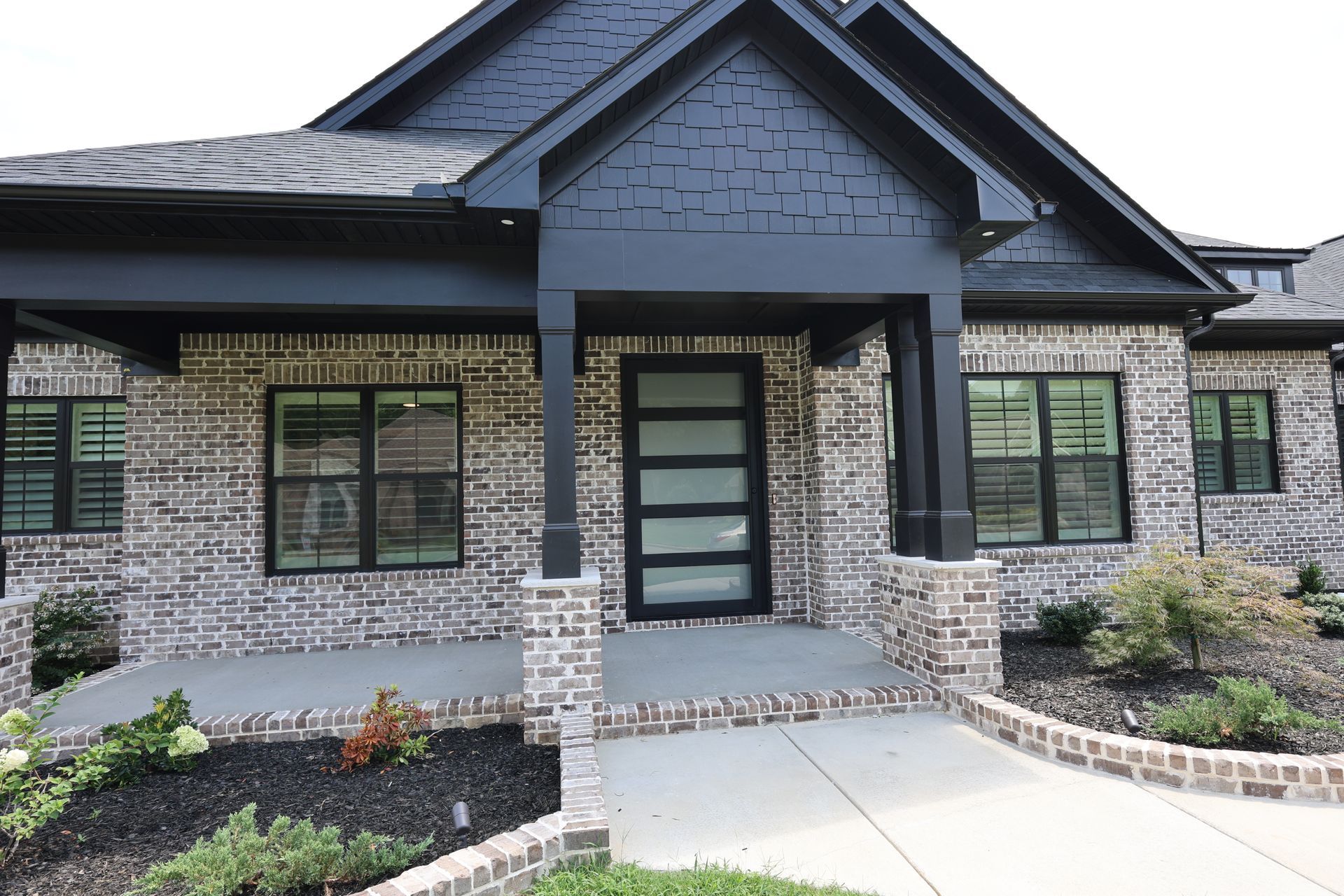 Modern brick house with black trim, porch, and glass front door.