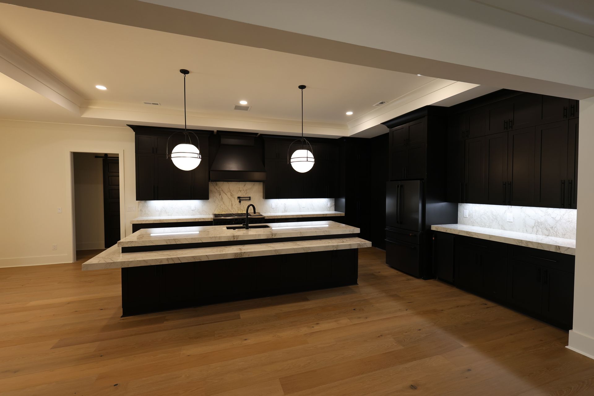 Modern black kitchen with island, white countertops, wood floors, and pendant lights.