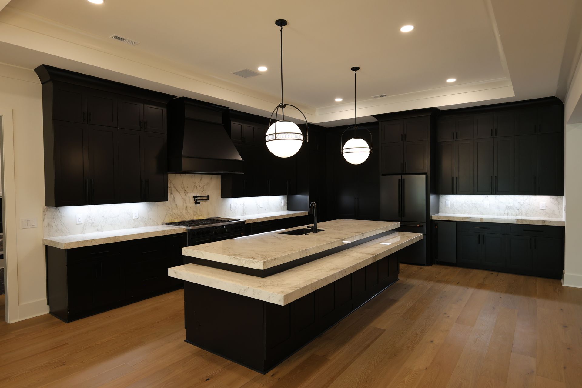 Modern kitchen with black cabinets, white countertops, and wood floor. Two globe pendant lights hang over the island.