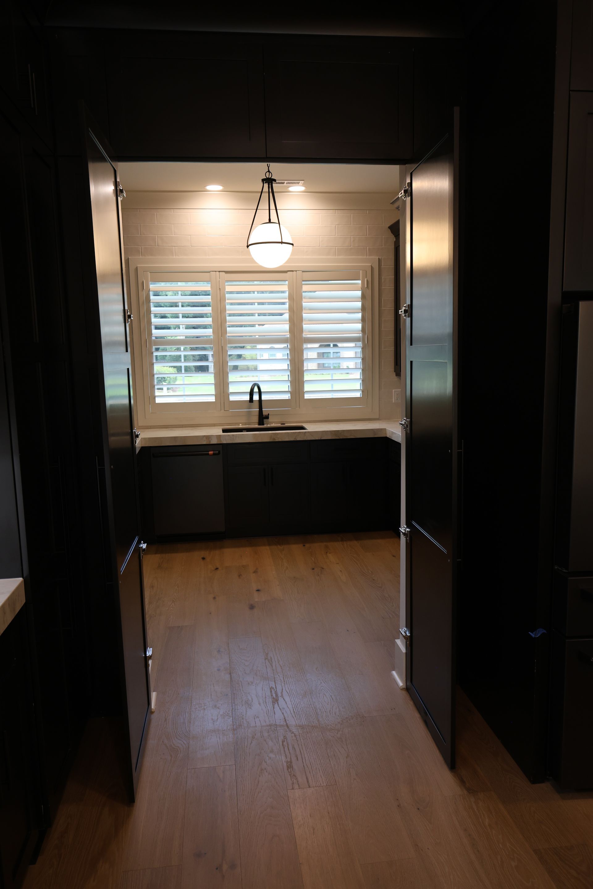 Dark doorway leading to a kitchen with cabinets, window, and pendant light.