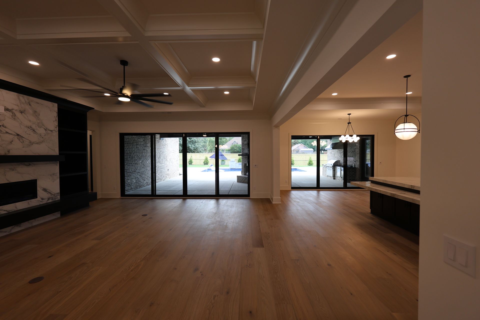 Spacious living area with wood floors, fireplace, and glass doors opening to a backyard with a pool.