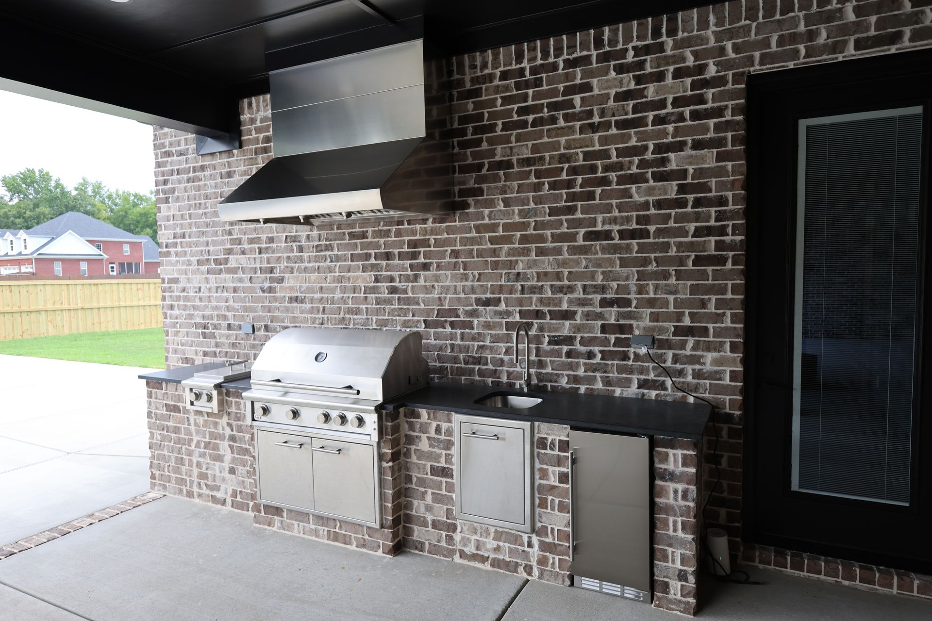 Outdoor kitchen with brick wall, stainless steel grill, sink, and refrigerator.