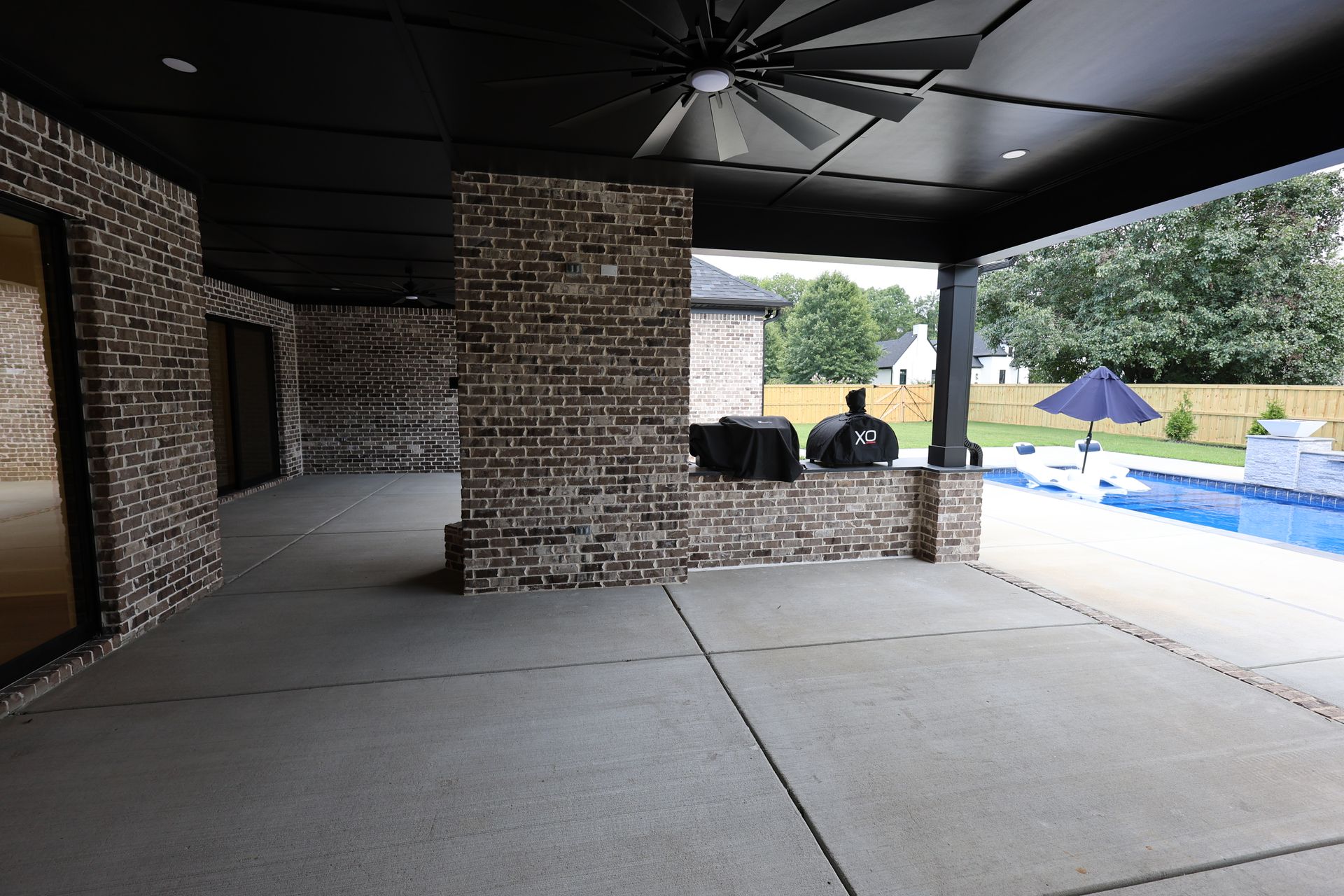 Covered patio with brick columns and ceiling fan, overlooking a pool.