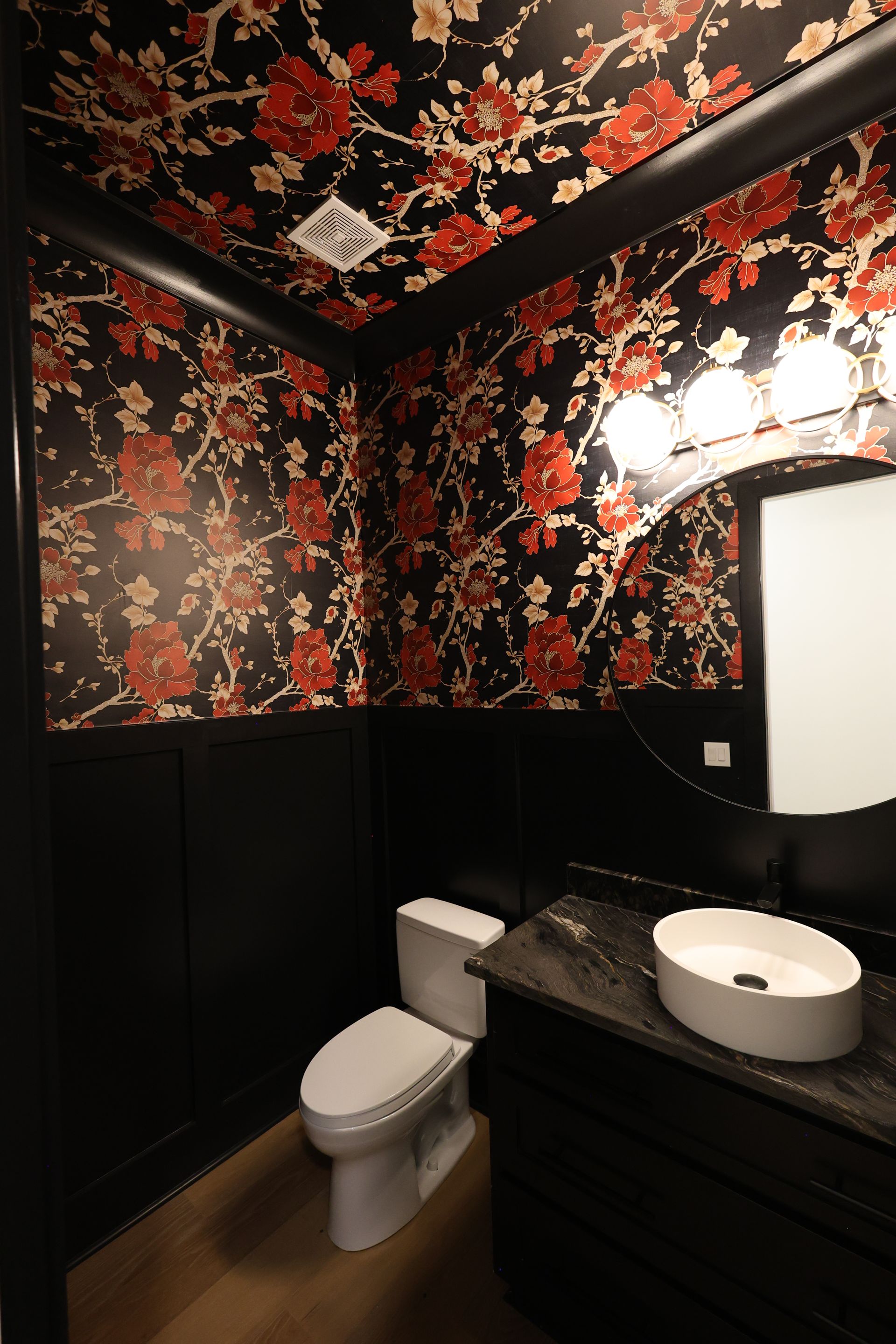 Powder room with floral wallpaper, black trim, toilet, and a vessel sink.