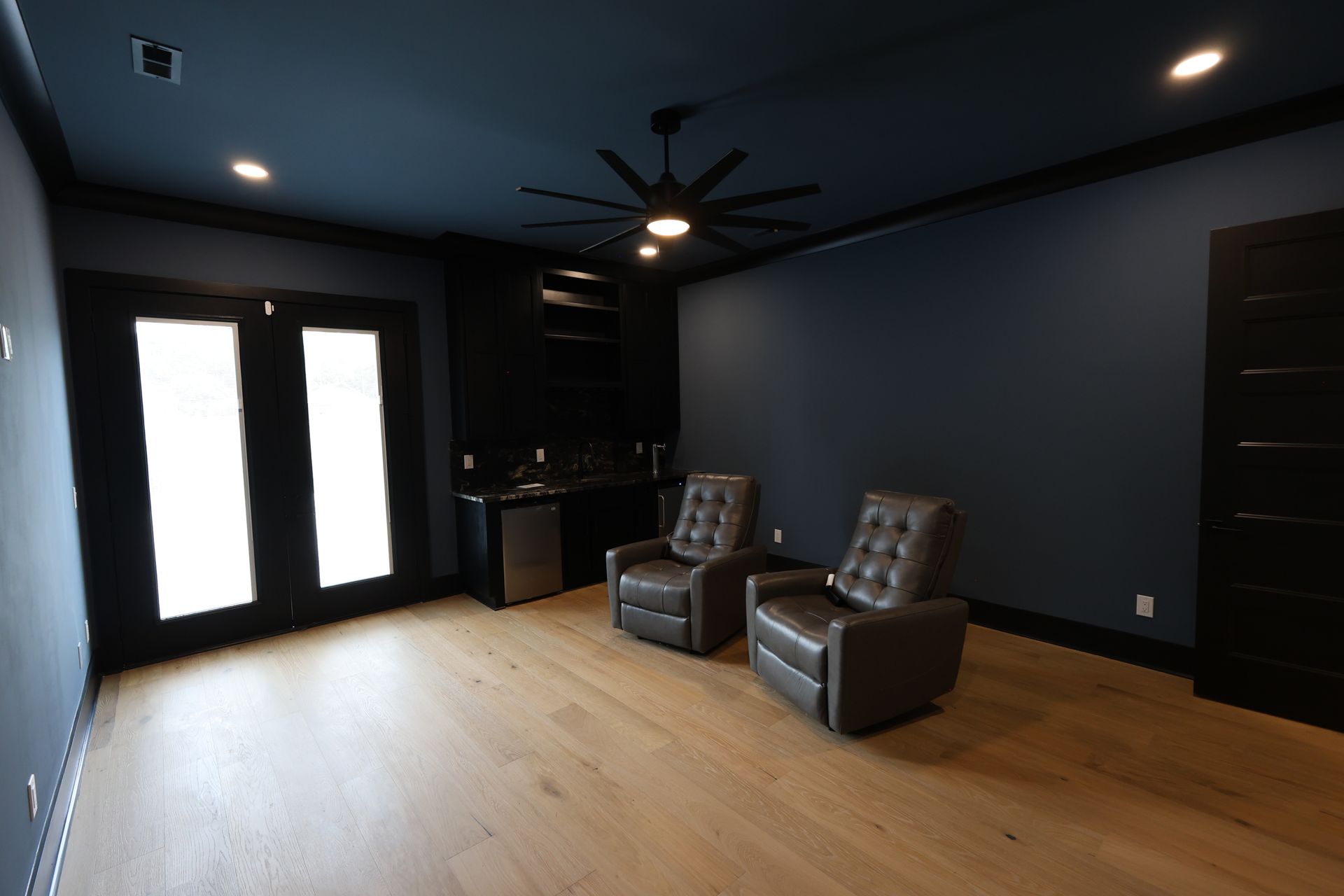 Dark blue home theater with two recliners, wood floor, and a black bar area.